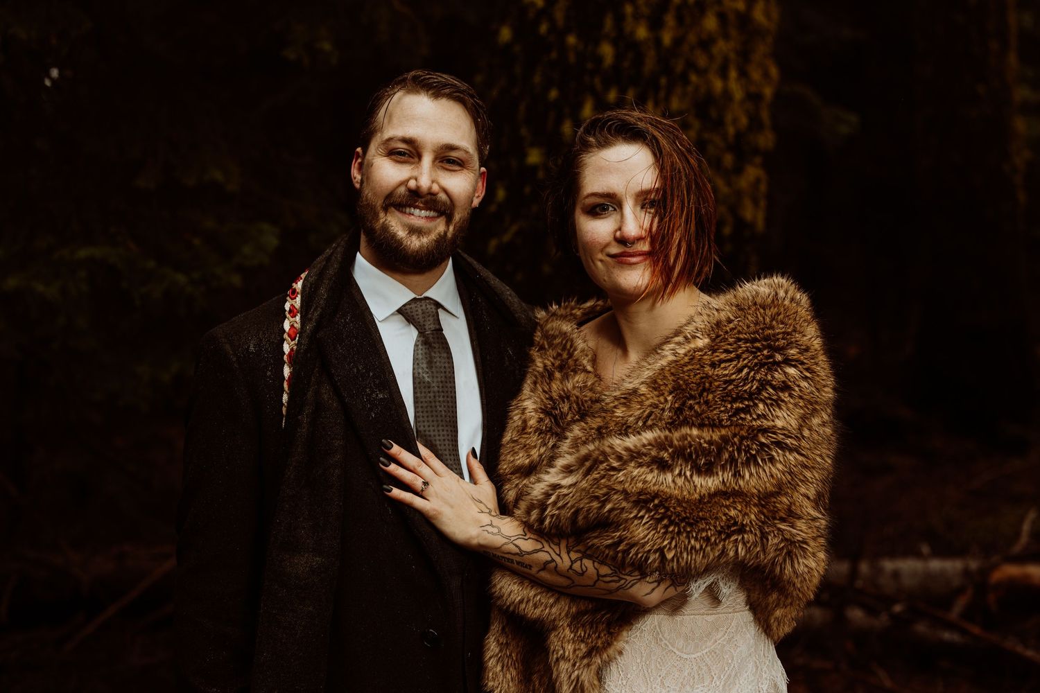 Newlyweds posing together in a forest, bride wearing a fur stole over her lace wedding gown.