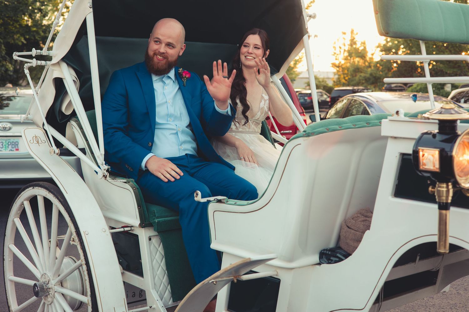 Smiling newlyweds wave from a classic white horse-drawn carriage at their wedding celebration.
