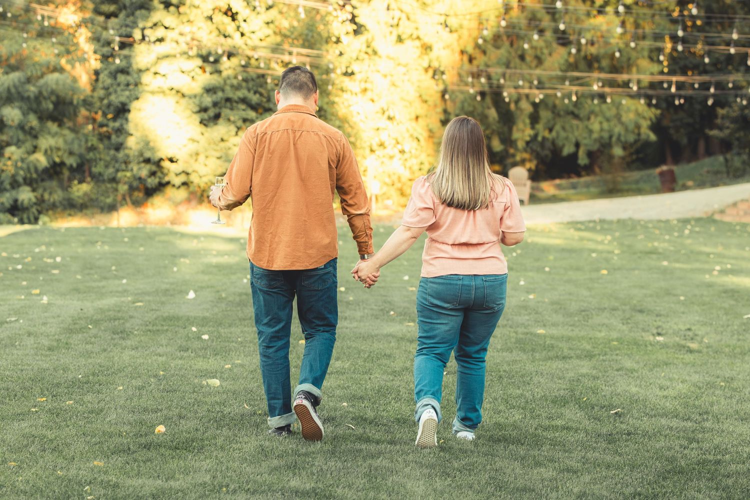 Rear view of a couple holding hands while strolling through a park with golden autumn foliage.