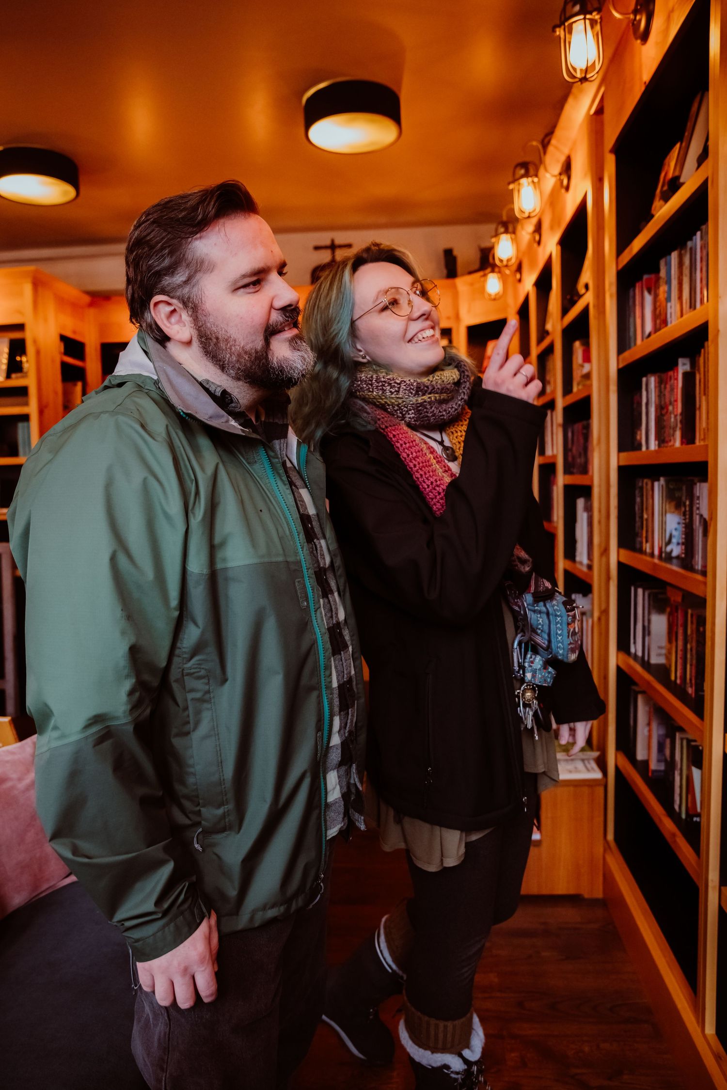 Couple browsing books together in a warmly lit independent bookstore with wooden shelves.