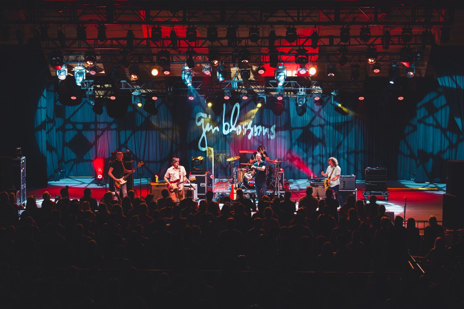 Jin Blossoms band performing on a large stage with colorful lights and a crowd of fans at a live concert.