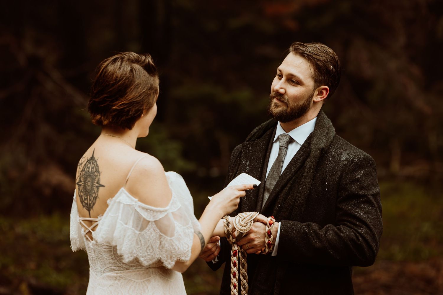 Bearded groom reads vows to bride during a rustic outdoor handfasting wedding in the forest.