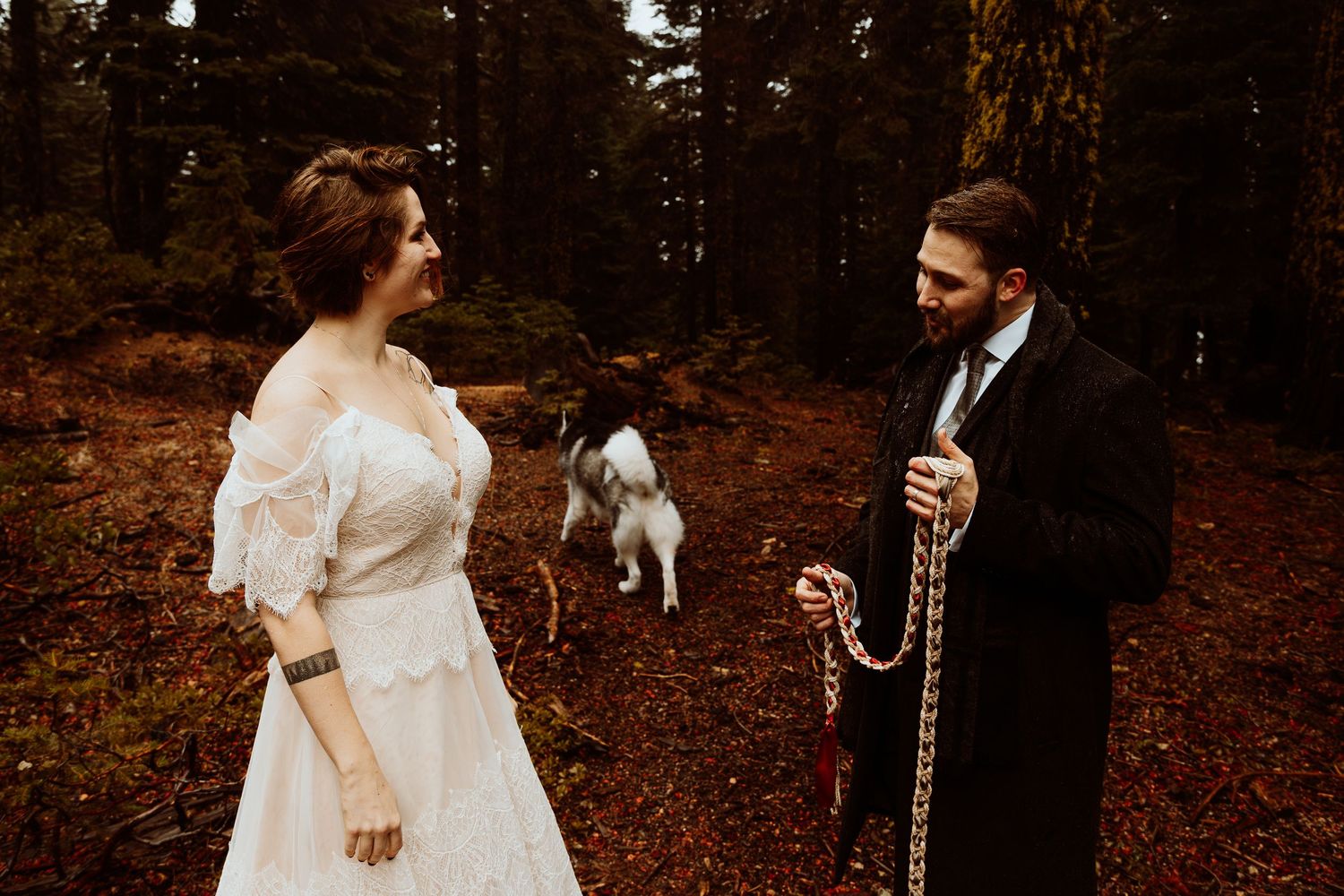 Bride and groom share a moment with their husky dog during a forest handfasting ceremony.