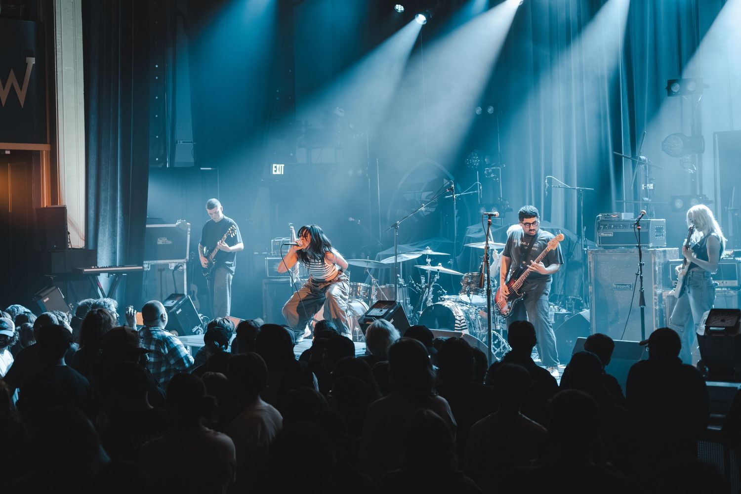 Live band concert with blue stage lighting as crowd watches energetic full band performance.