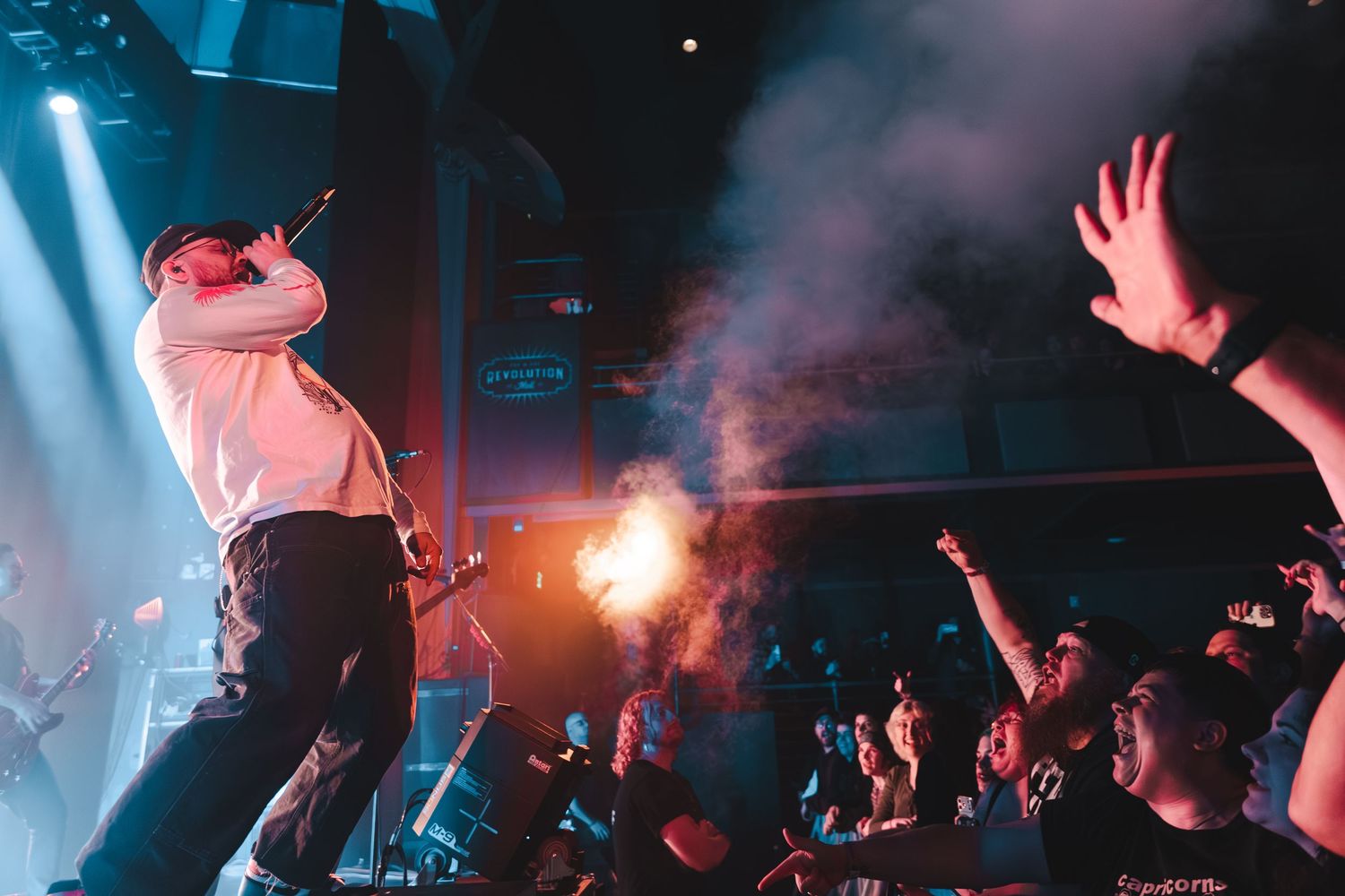 Rock singer performs with pyrotechnics and smoke effects as fans reach up at a live show.