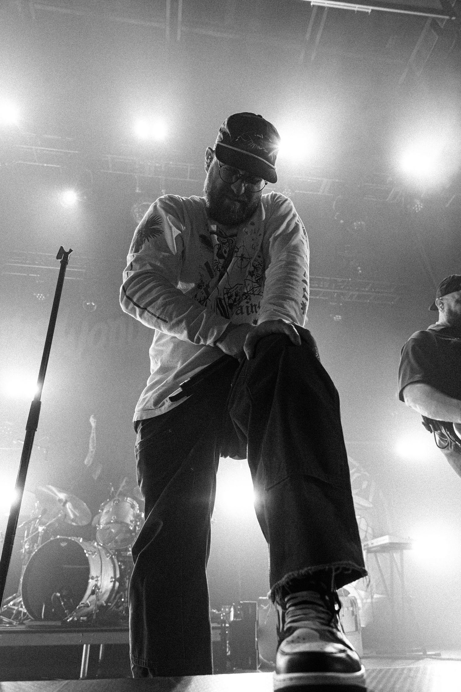 Black and white photo of a bearded performer in a beanie crouching on stage during a live concert.