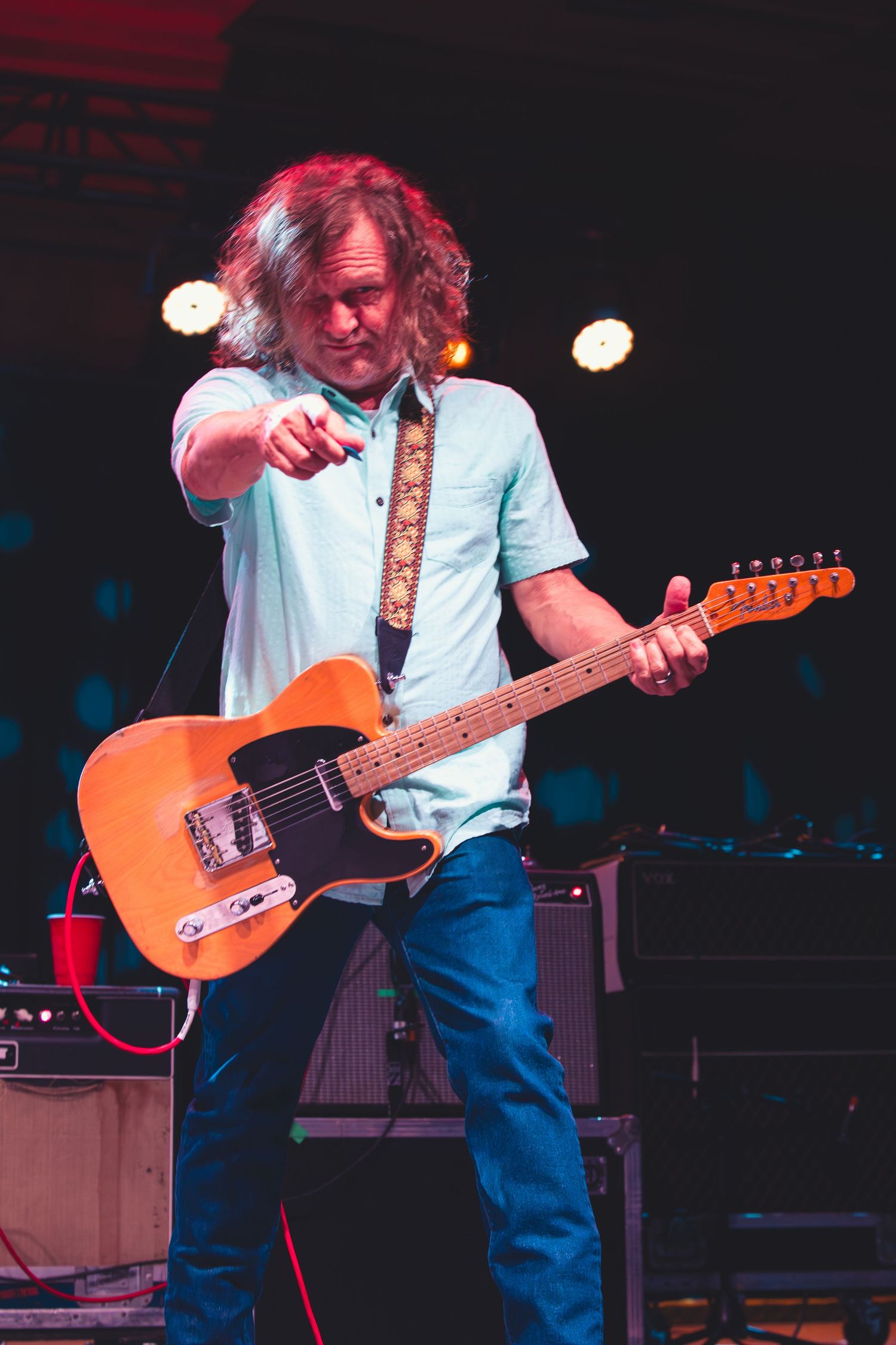 Guitarist points to the crowd while playing an orange Fender Telecaster on a live stage.
