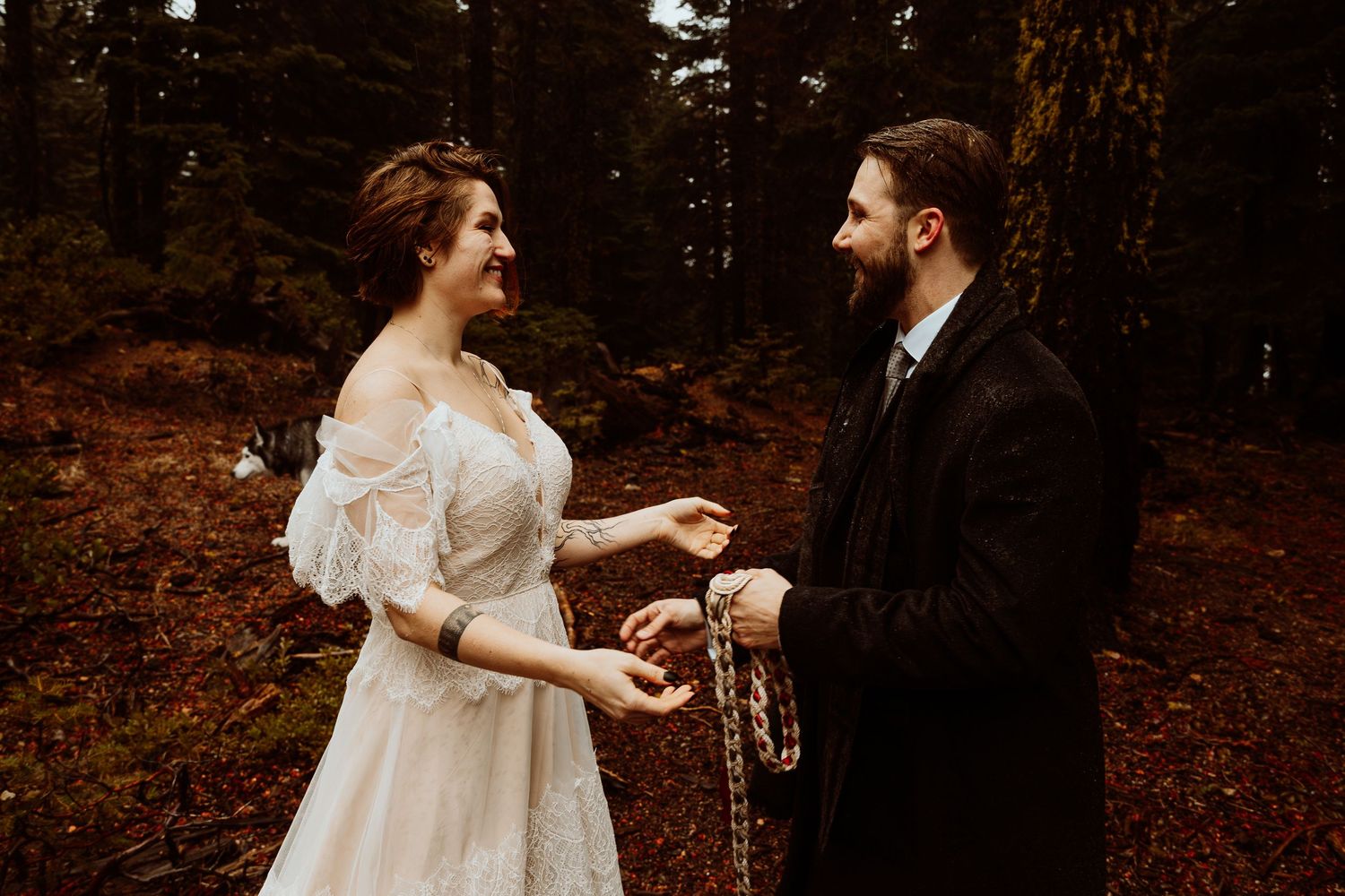 Couple smiling joyfully while holding a handfasting braid during their woodland wedding.