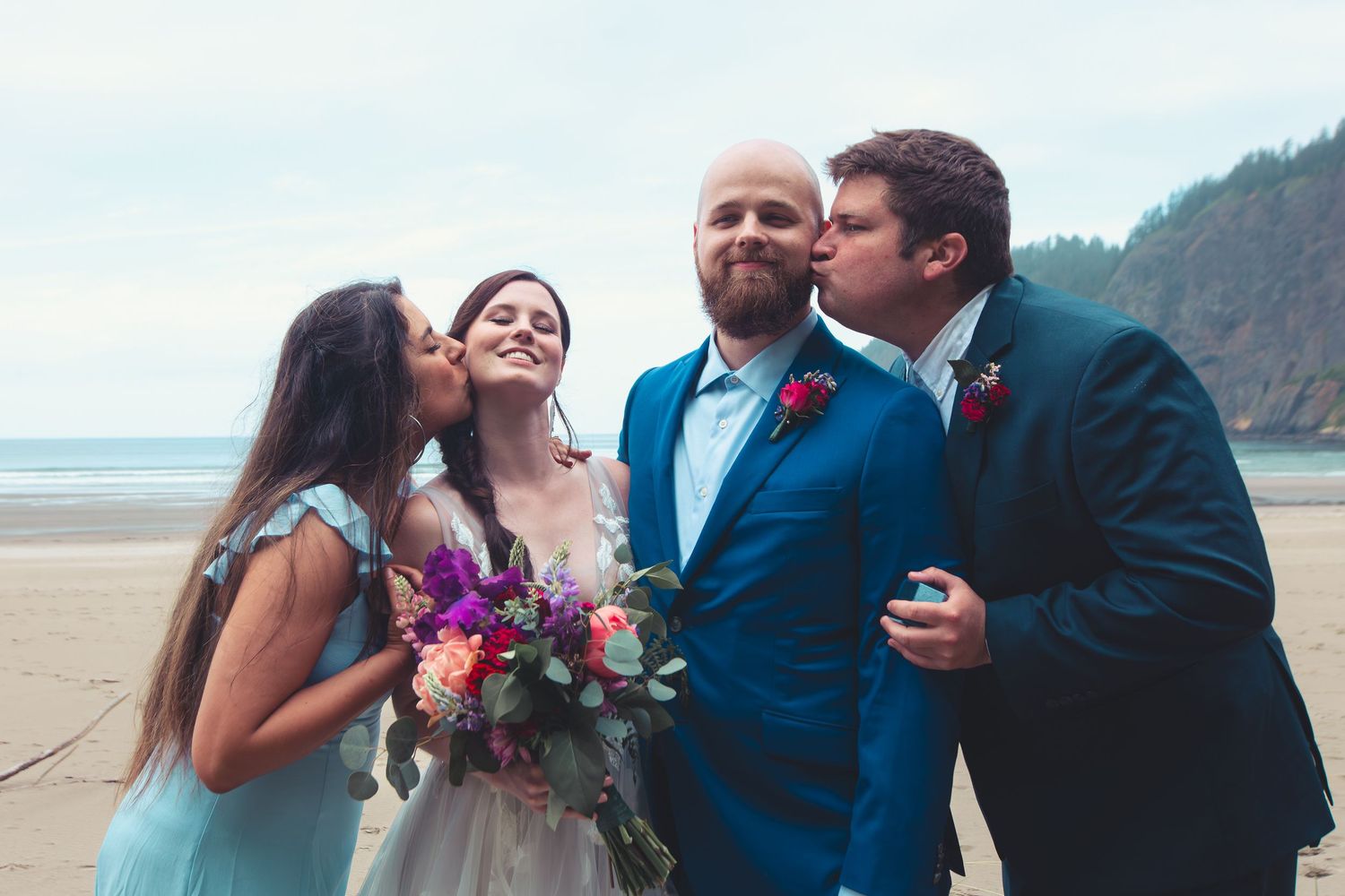 Bride and groom kissed on cheeks by bridesmaid and groomsman on a sandy beach wedding.