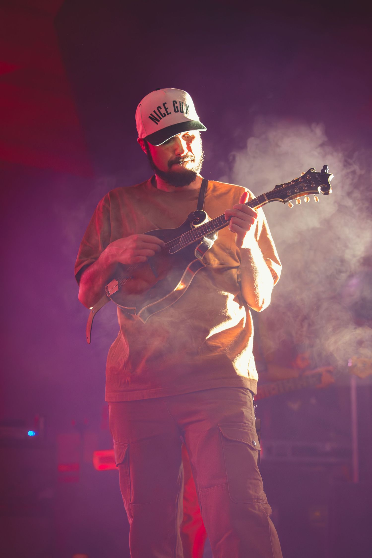 A bearded musician plays mandolin on stage surrounded by atmospheric smoke and purple lighting.