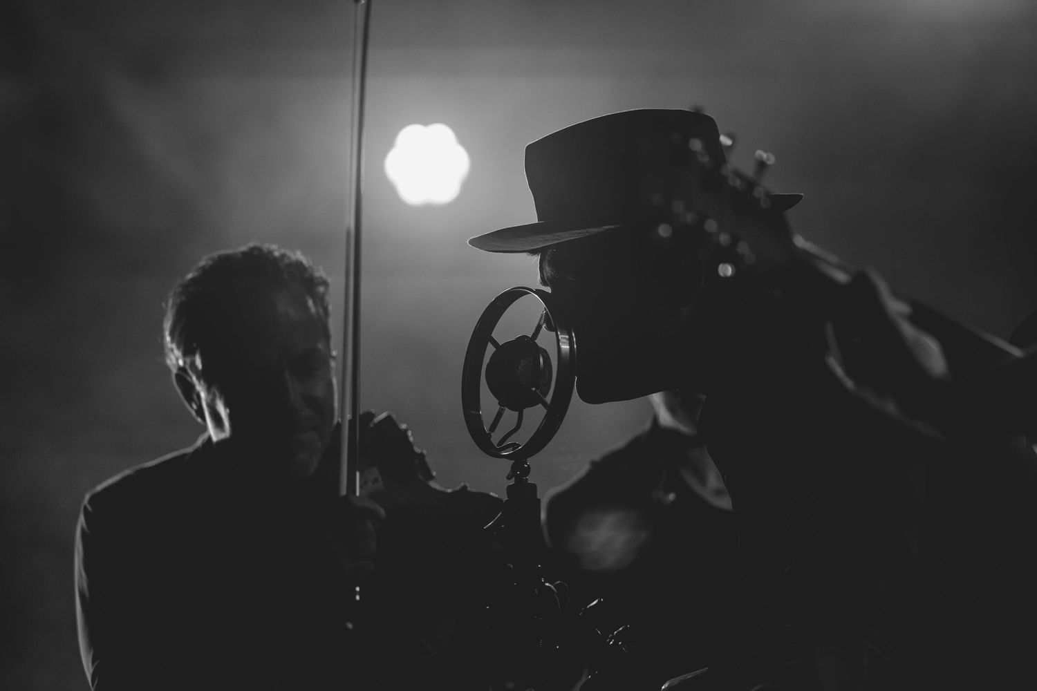 Black and white photo of two musicians performing on stage with a vintage ribbon microphone.