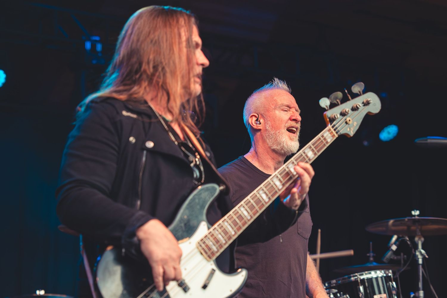 Two musicians playing bass guitars together on a dark concert stage.