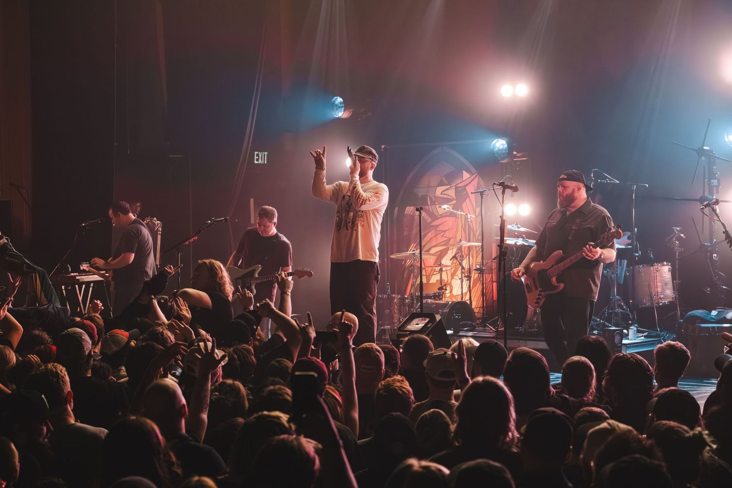 Live band performance with vocalist raising hands before an enthusiastic concert crowd.