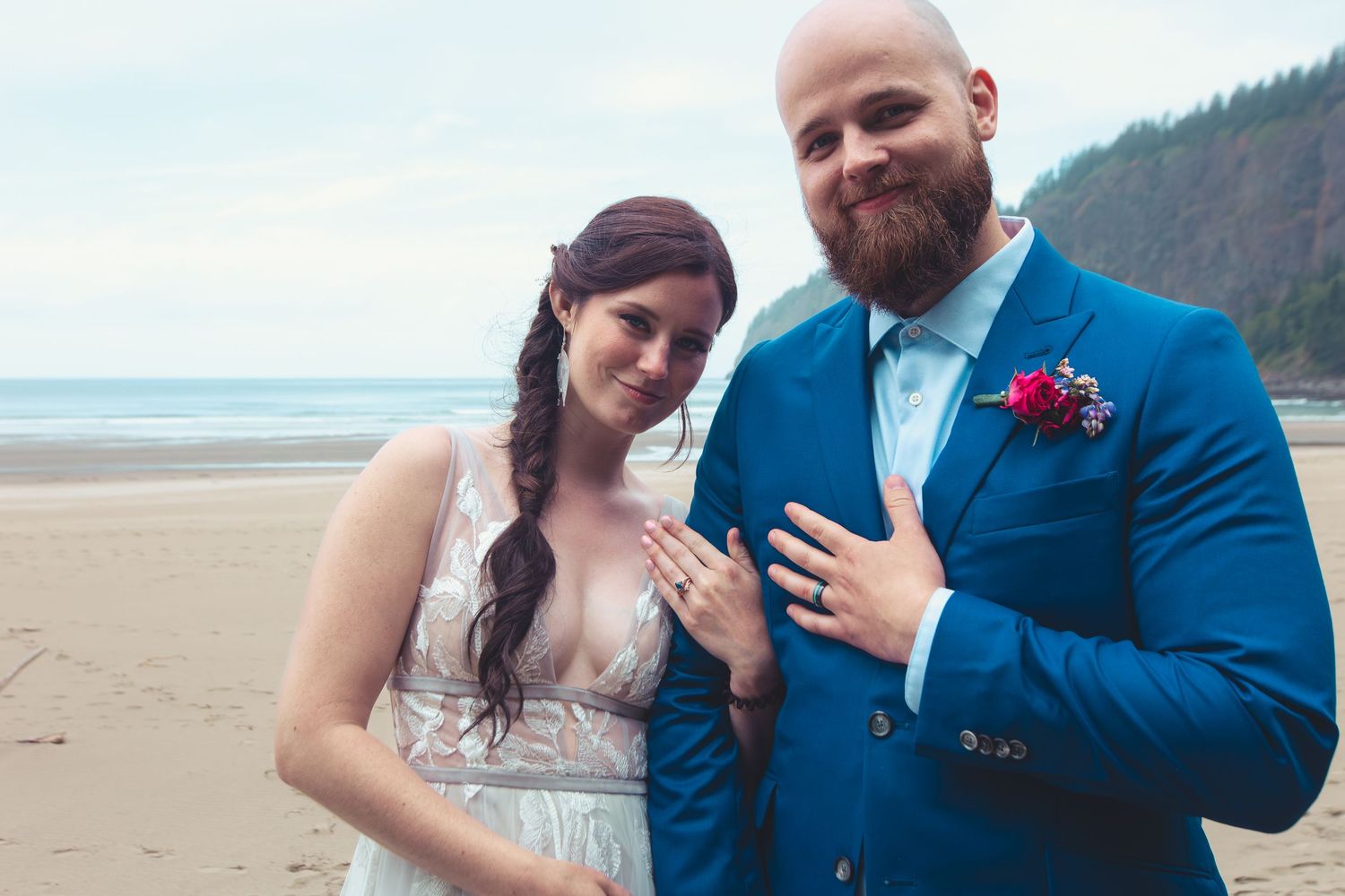 Newlywed couple proudly displays wedding rings on a sandy beach after their seaside ceremony.
