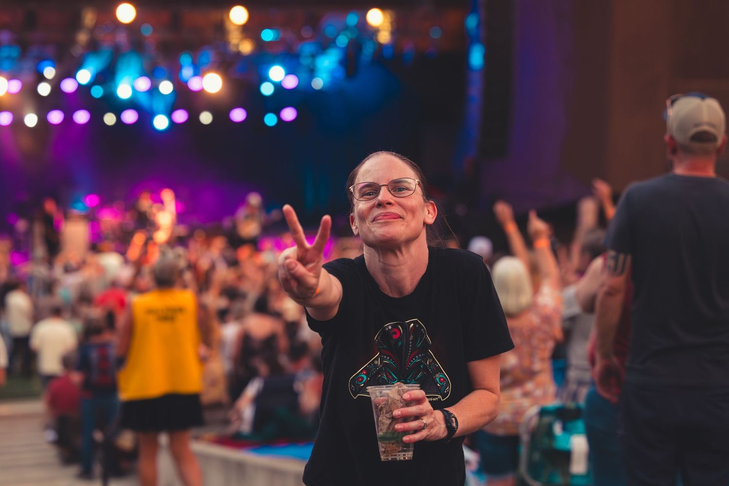 Smiling woman making a peace sign at a colorful outdoor music festival.