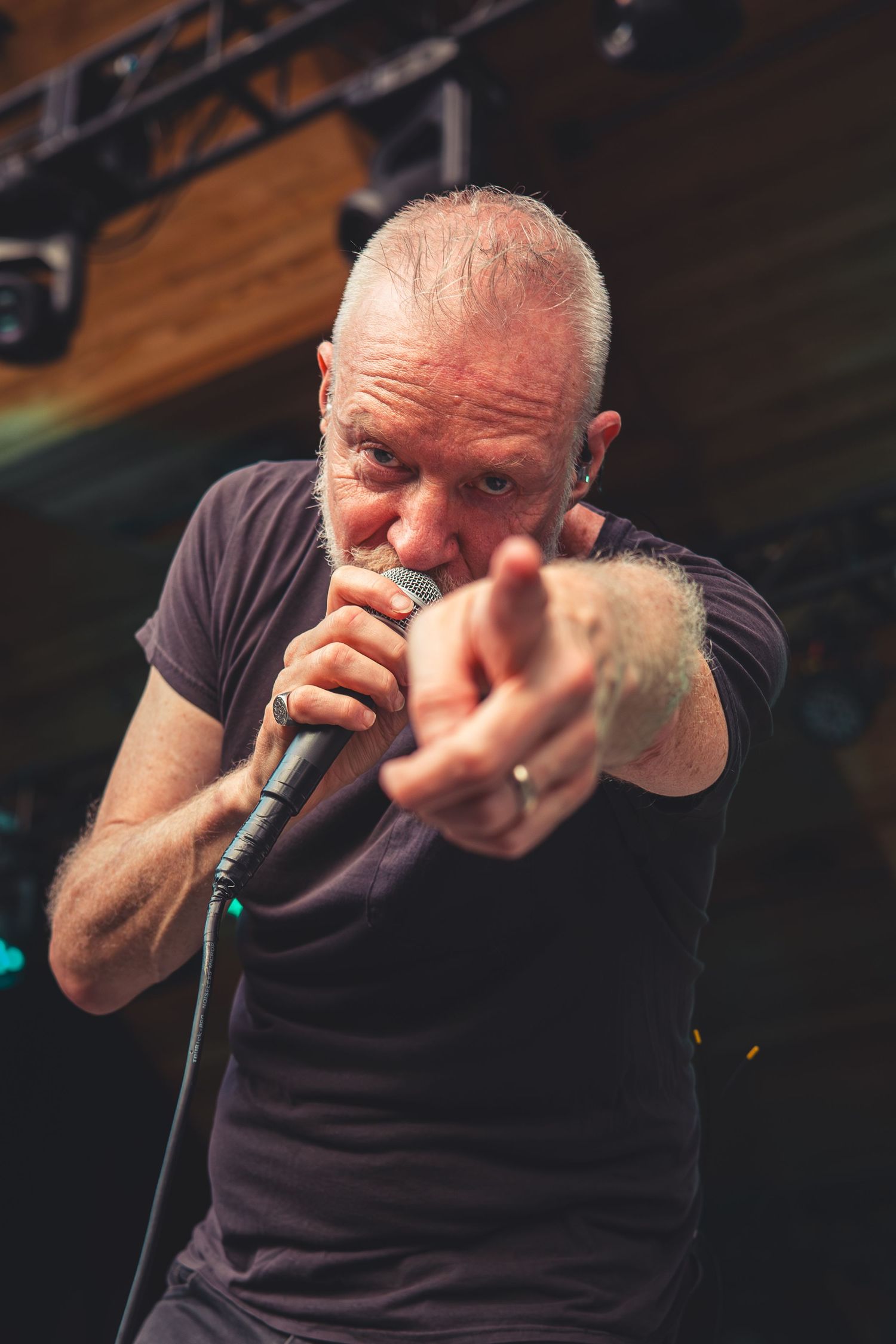 Bald male singer performing on stage, holding microphone and pointing at audience with intensity.