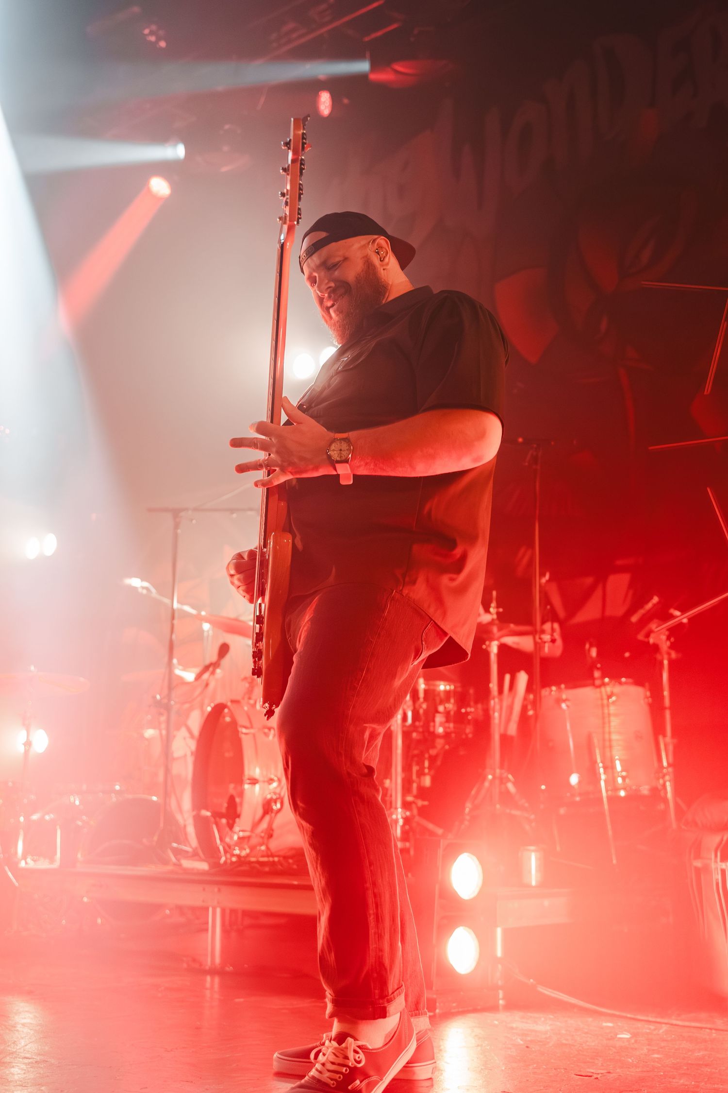 Bass guitarist performing on stage bathed in red concert lighting.