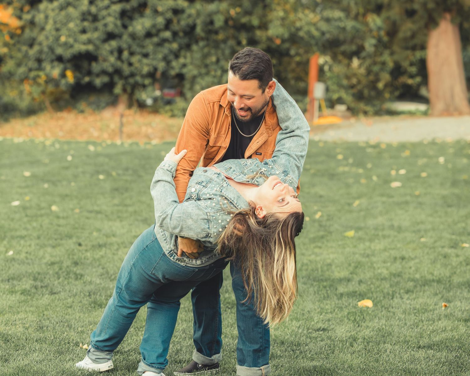Man playfully dipping woman while laughing together on a grassy lawn.