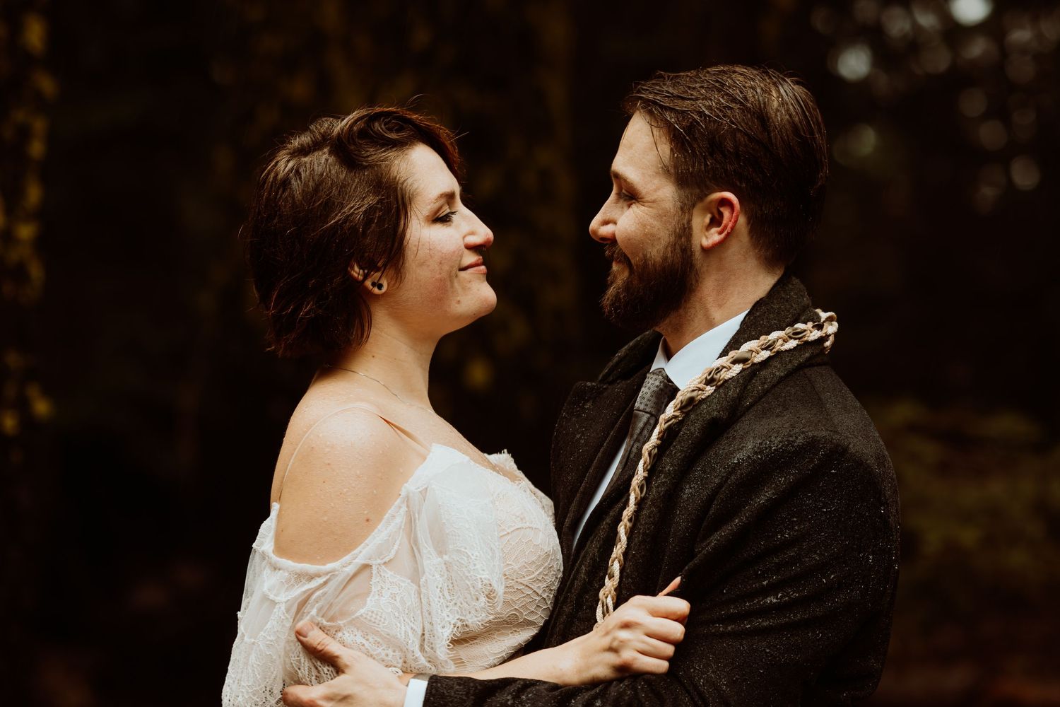 Bride and groom gazing lovingly at each other in a dark autumn forest wedding portrait.