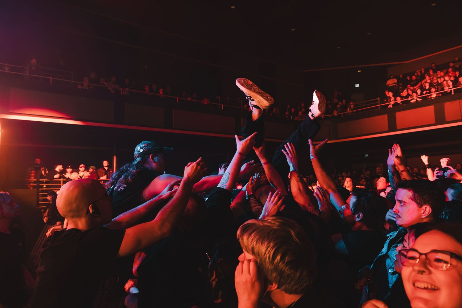 Crowd surfing at a packed live concert with fans reaching up to help.