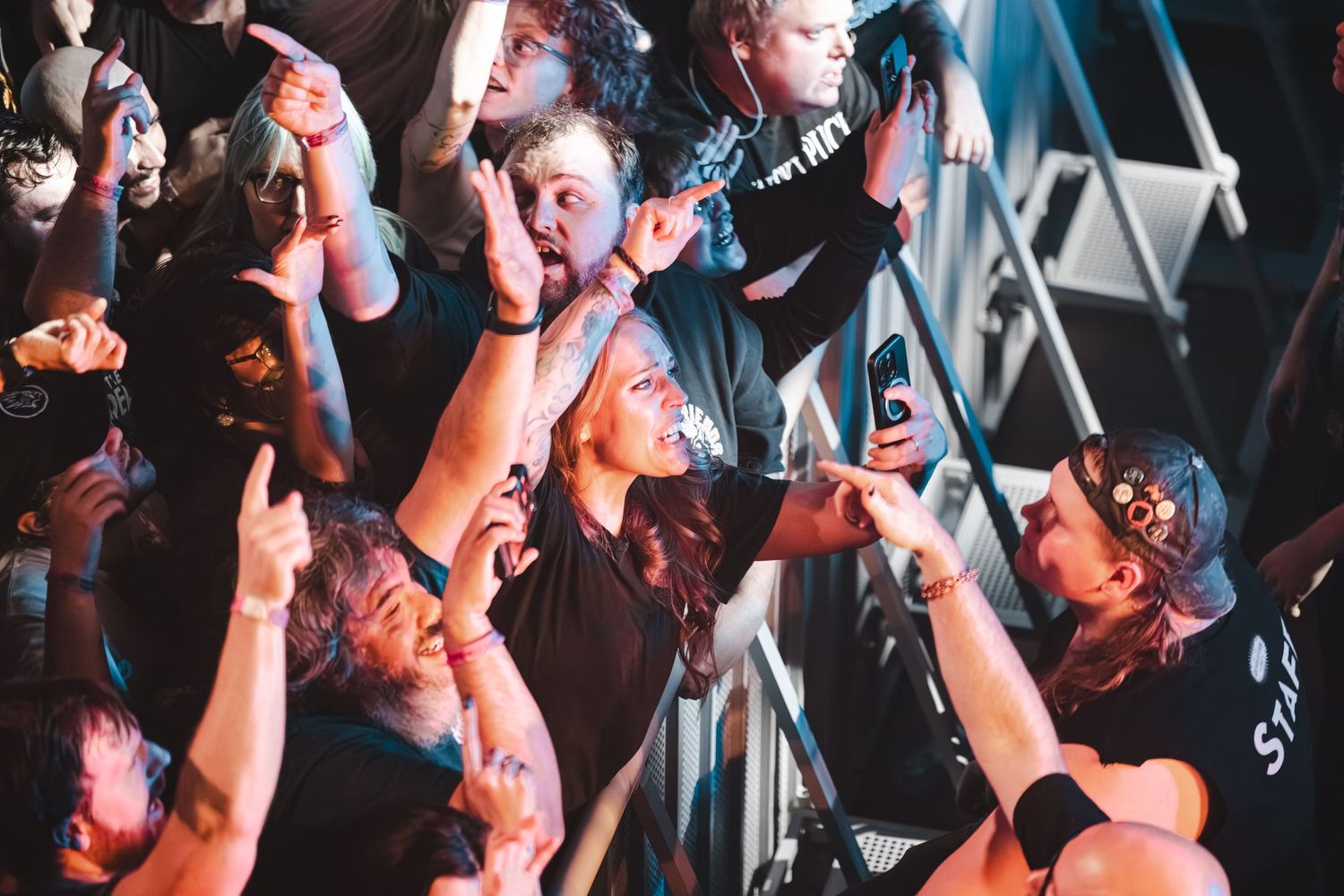 Excited concert crowd cheering and raising hands at a live rock music event.