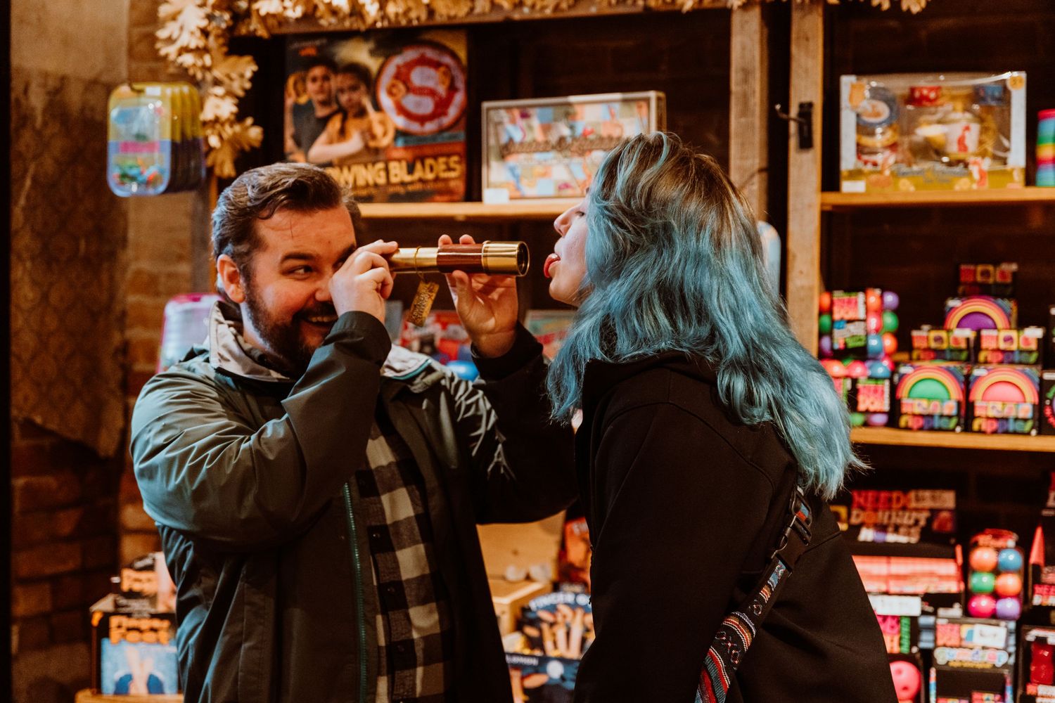A man and woman with blue hair playfully interact in a colorful fireworks shop.