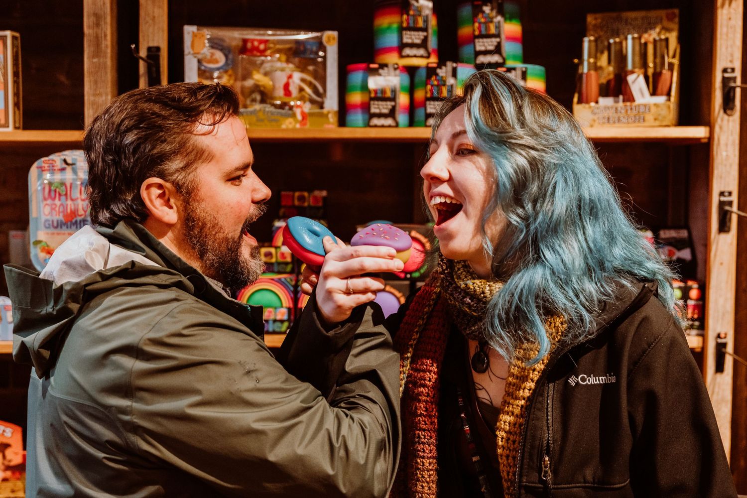 Couple playfully sharing a colorful donut in a vibrant candy shop.