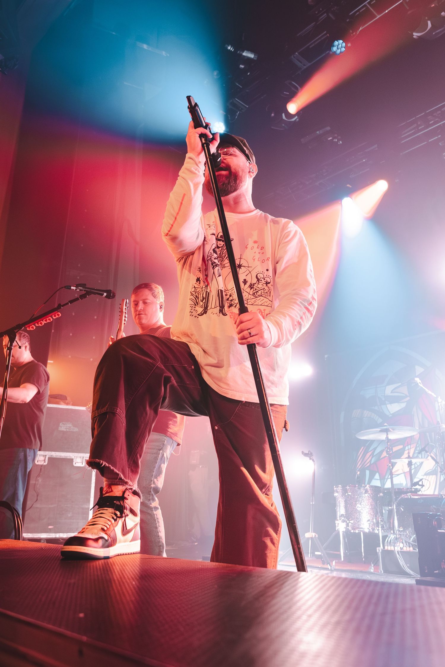 Male vocalist performing on stage holding microphone stand under colorful concert lights.