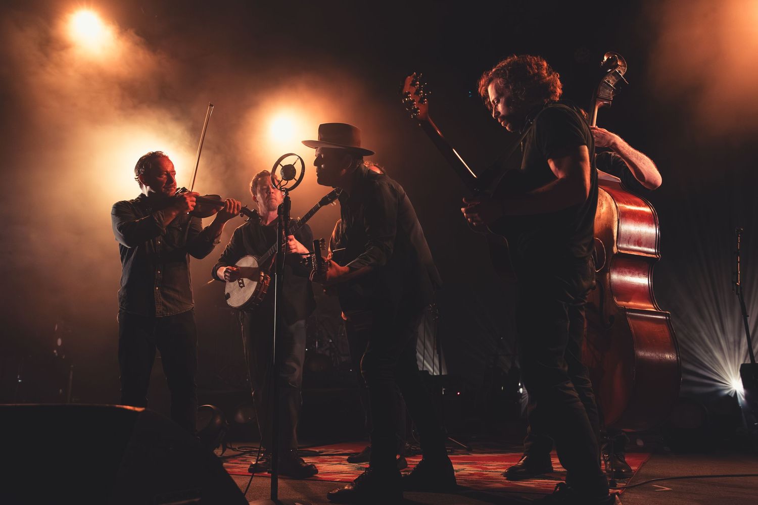 Folk band with violin, banjo, and double bass performs under warm stage lights.