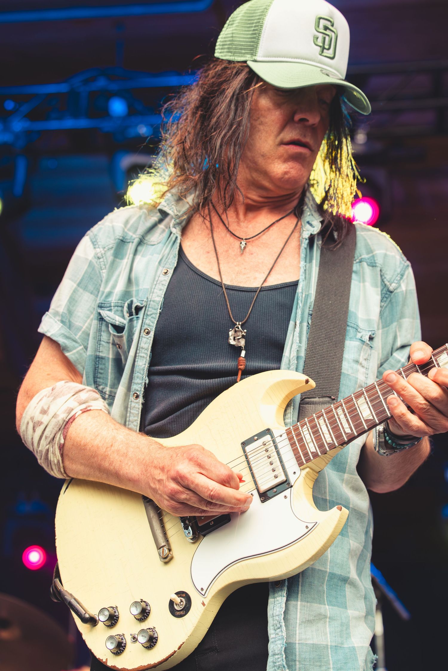 Long-haired guitarist playing a white Gibson SG electric guitar on stage.