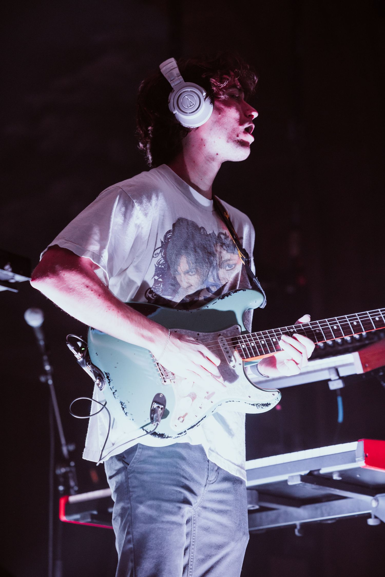 Young male guitarist wearing headphones plays Stratocaster guitar on stage.