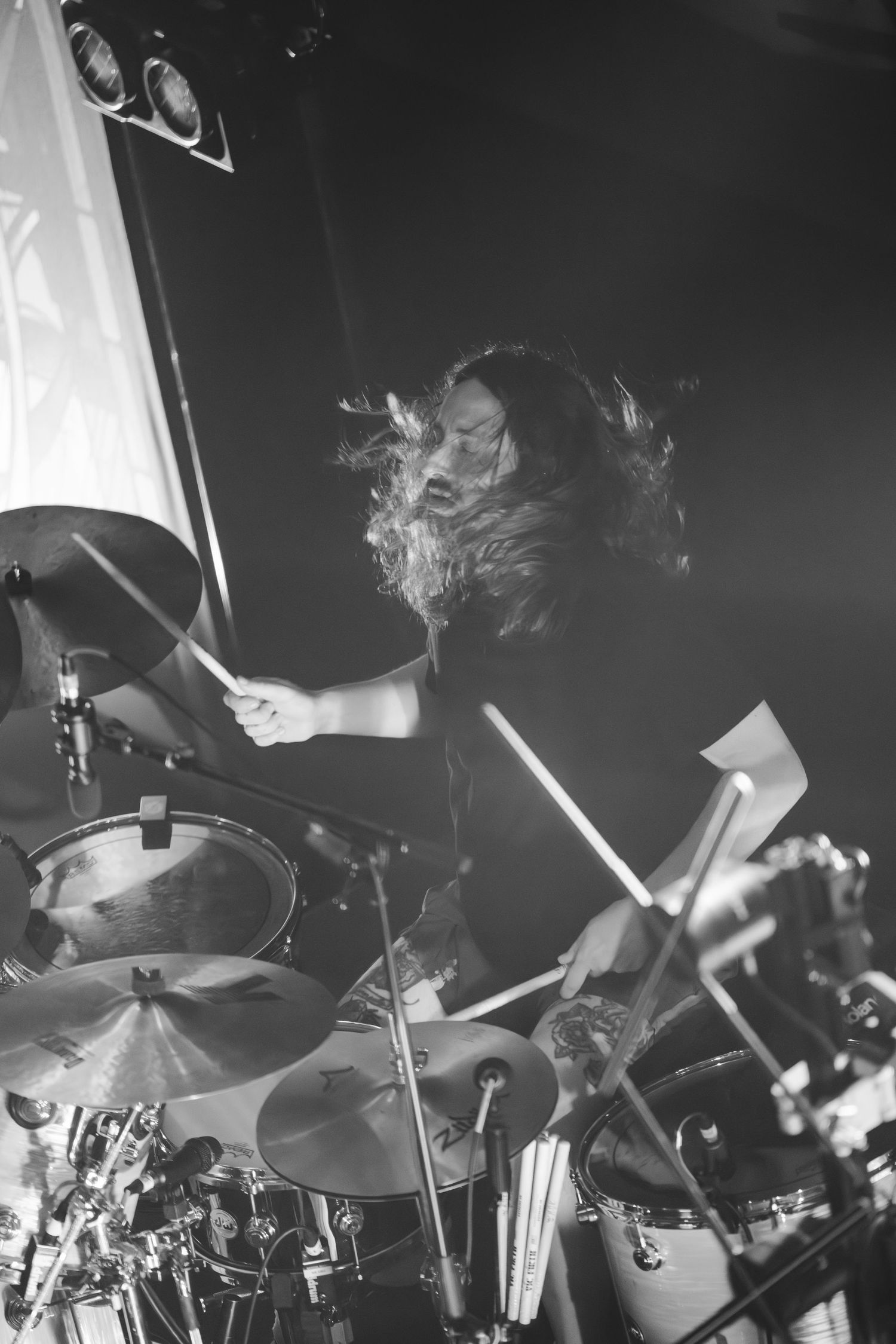 Black and white action shot of a drummer with flying hair performing energetically on stage.