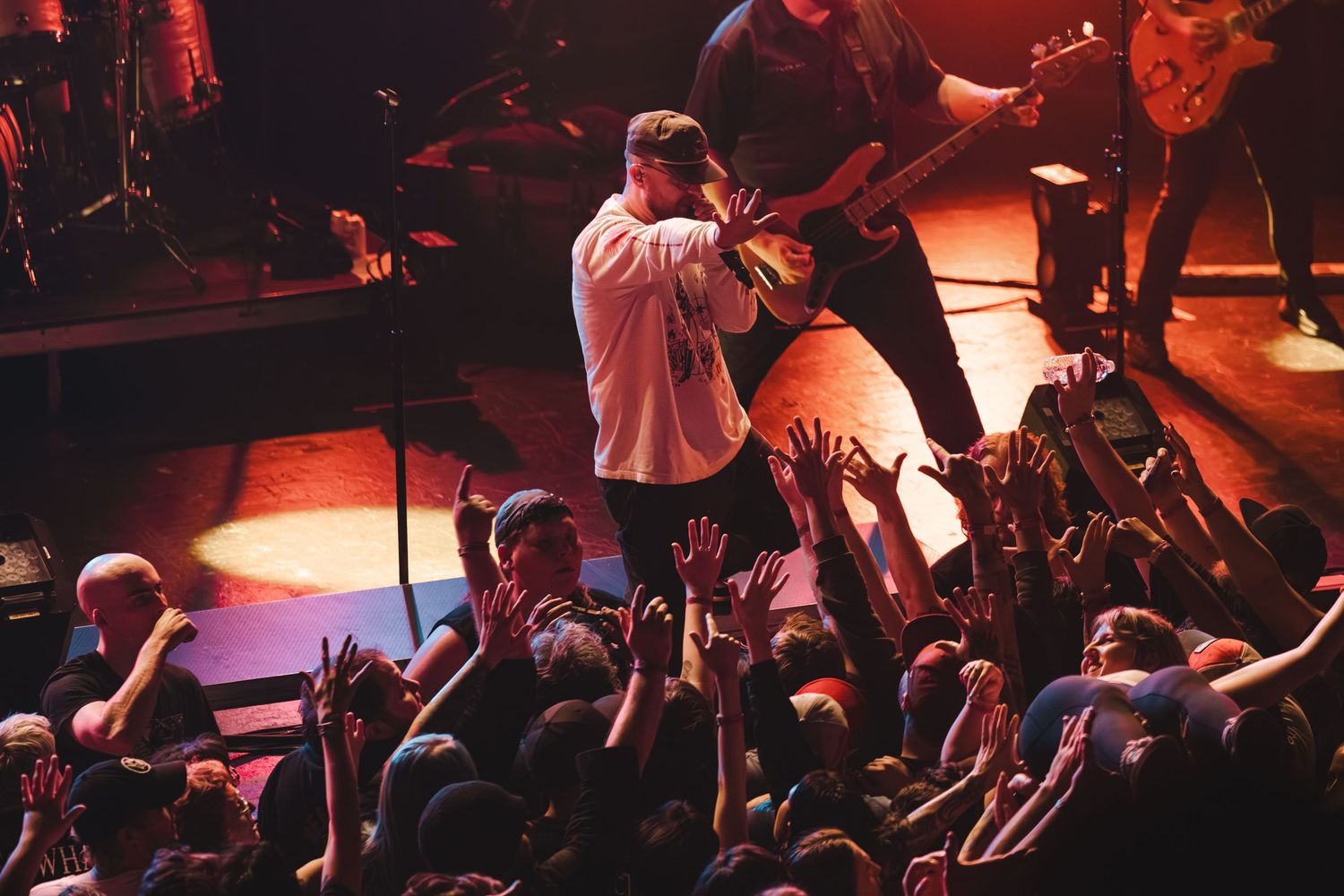 Singer performs on stage engaging with crowd of fans with raised hands at a live rock concert.