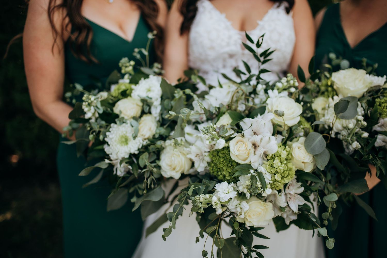 Elegant white and green wedding bouquets with roses and trailing greenery against dark dresses.
