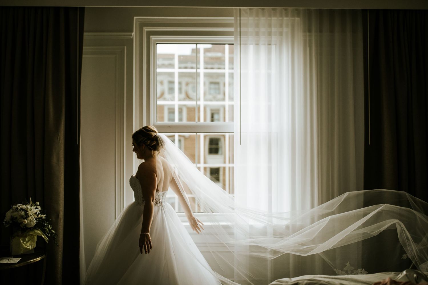 A flowing wedding gown silhouetted against a bright window creating a romantic atmosphere.