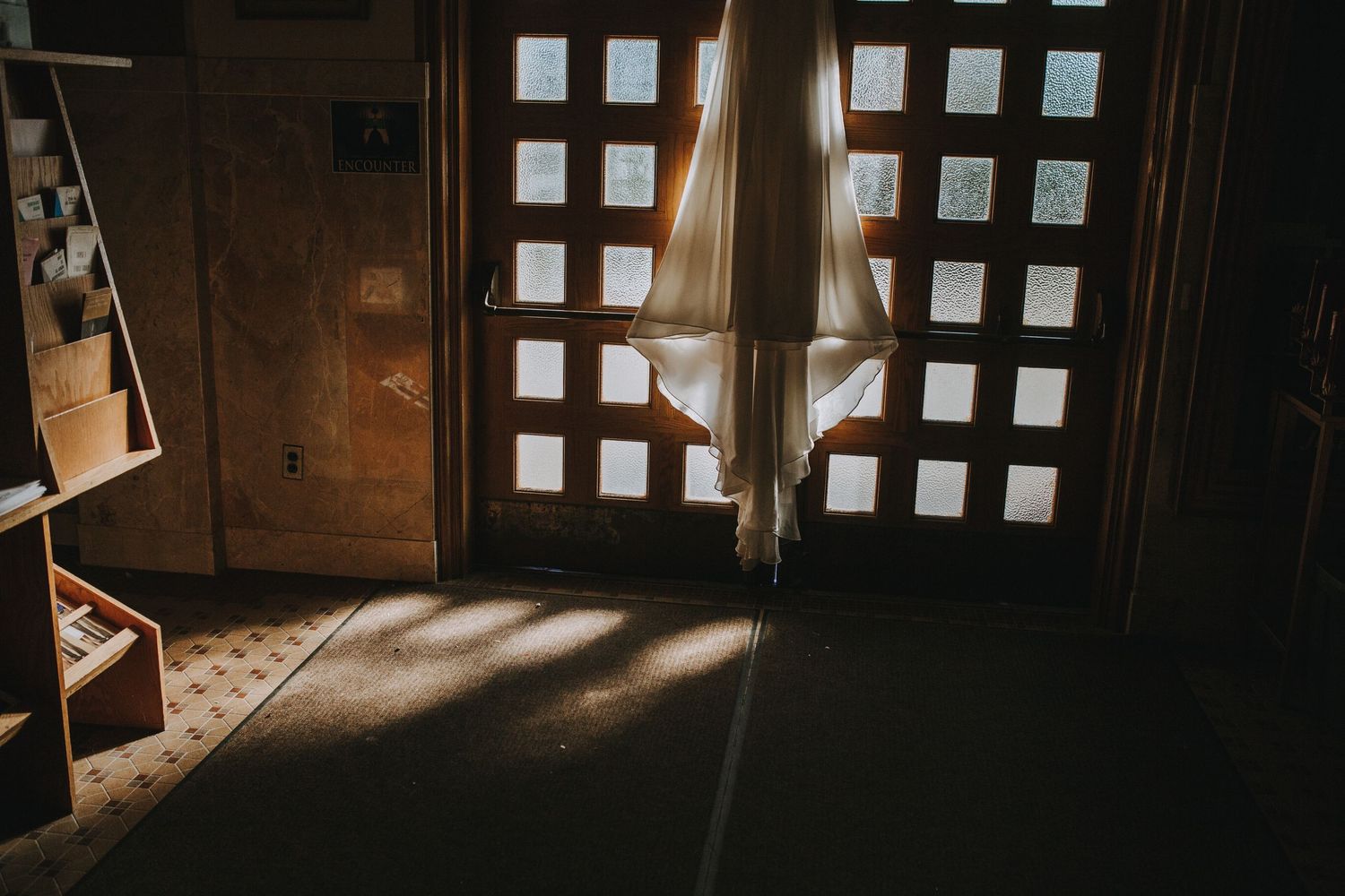 Sunlight streams through wooden window shutters in a dark rustic room creating dramatic shadows and light patterns.