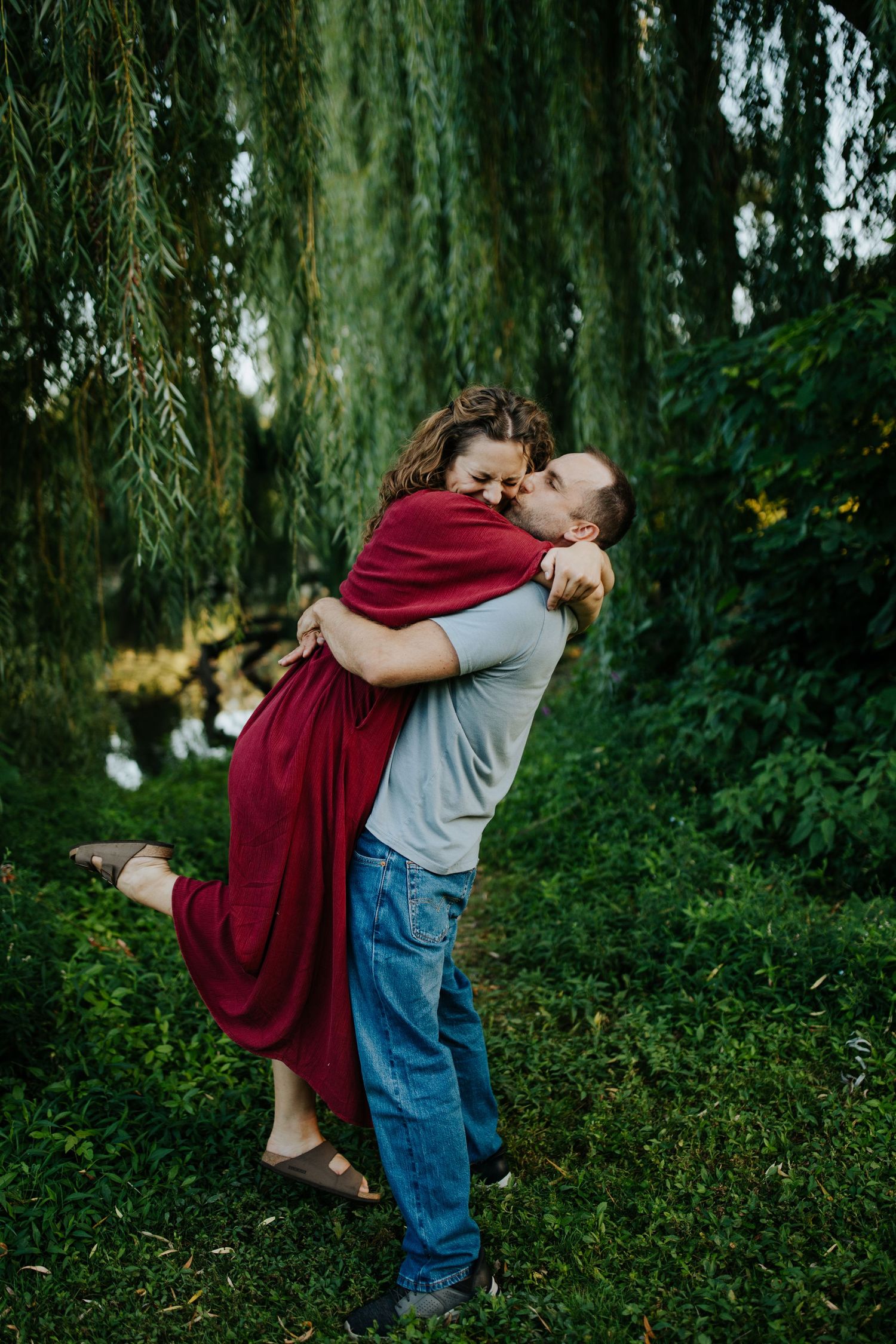 Romantic couple embracing under willow trees in a dreamy outdoor setting.