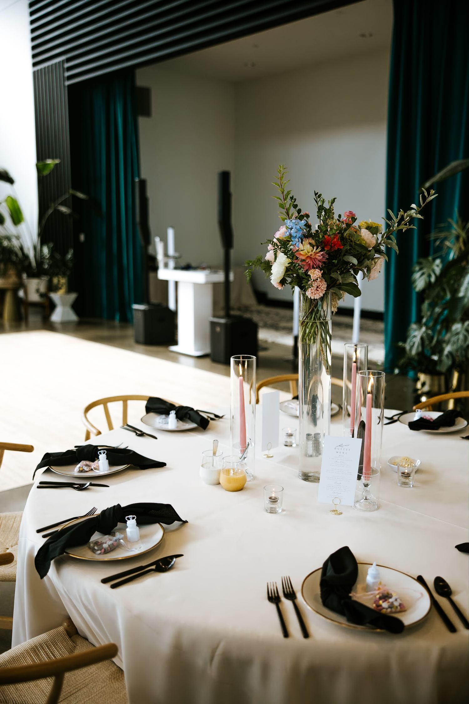 Elegant wedding table setting with black napkins, white linens, and colorful floral centerpiece.