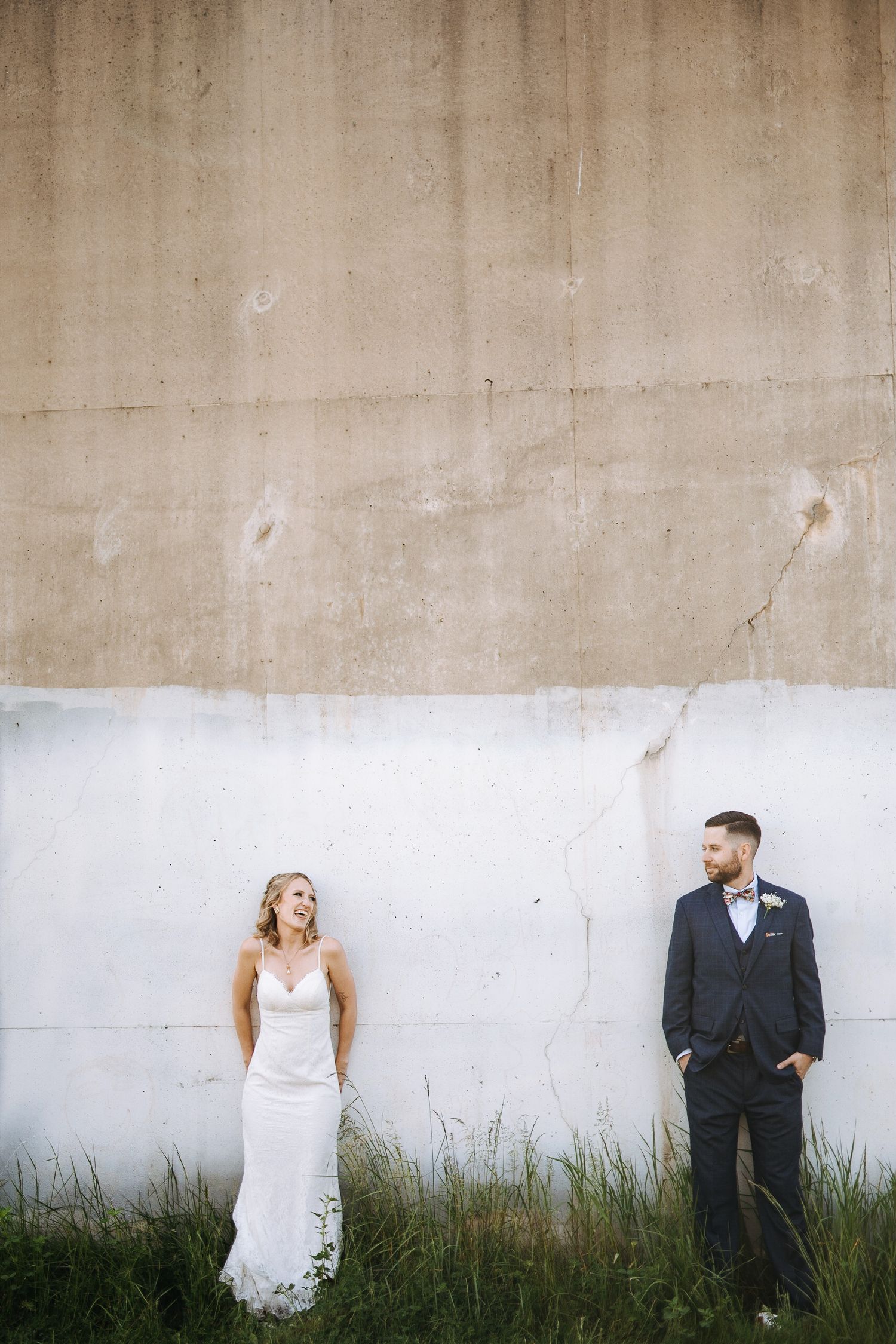 Artistic wedding portrait sequence against white concrete wall with growing grass at base.