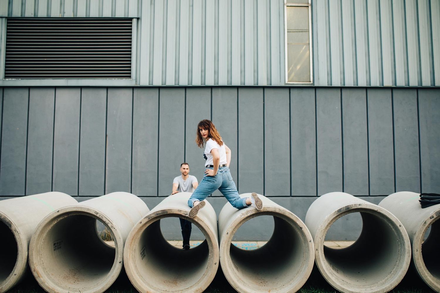 Industrial setting with concrete pipes and metal siding creating geometric patterns.