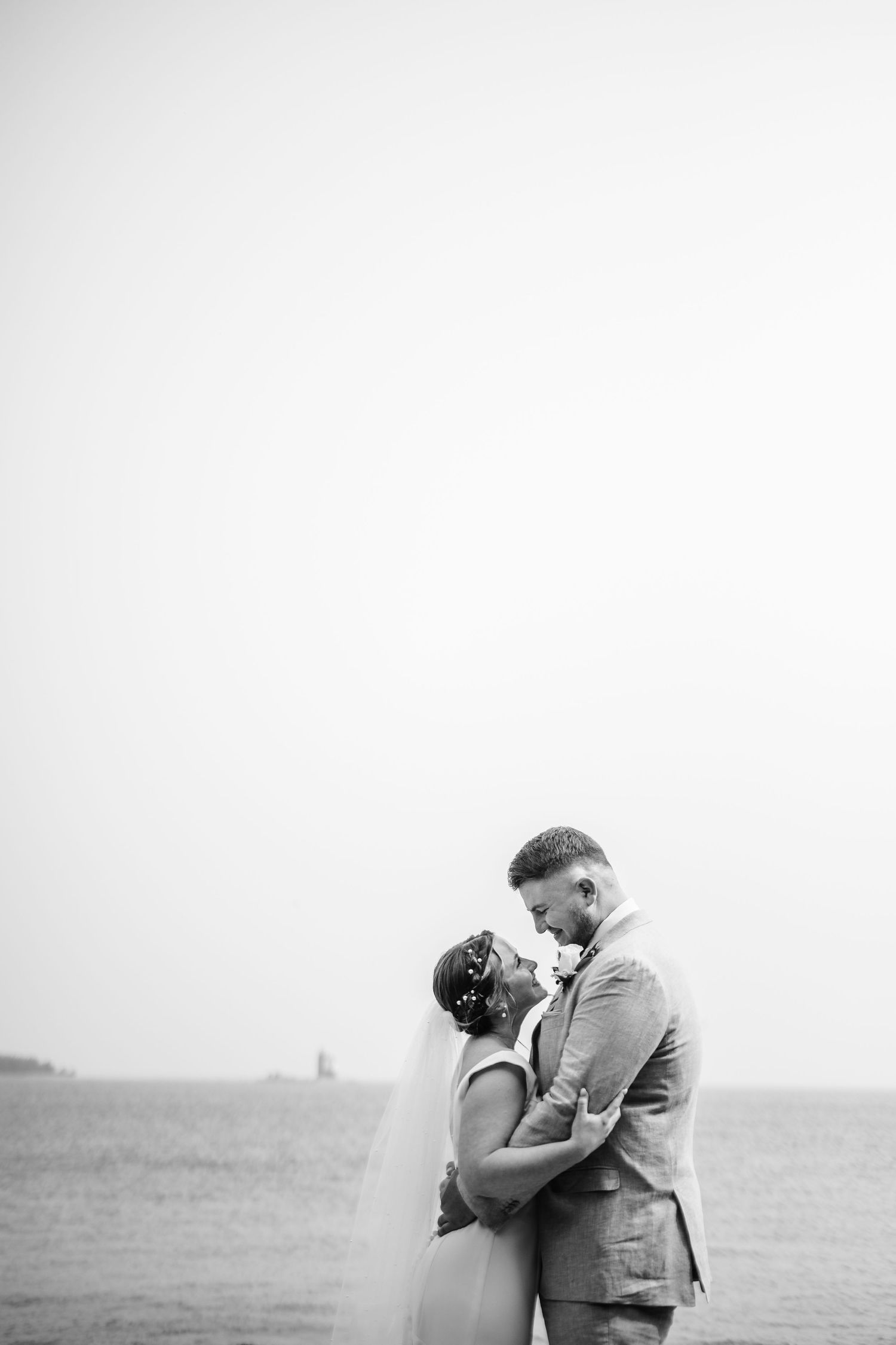 A romantic black and white wedding portrait captured against an overcast sky.