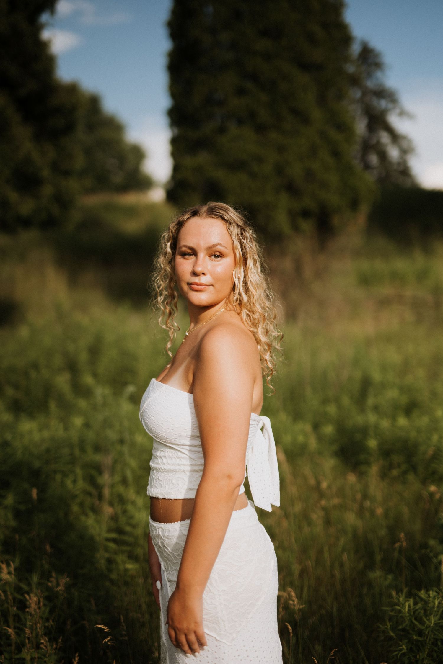 A series of outdoor portrait photographs in a field at golden hour showing a white dress against a natural backdrop.