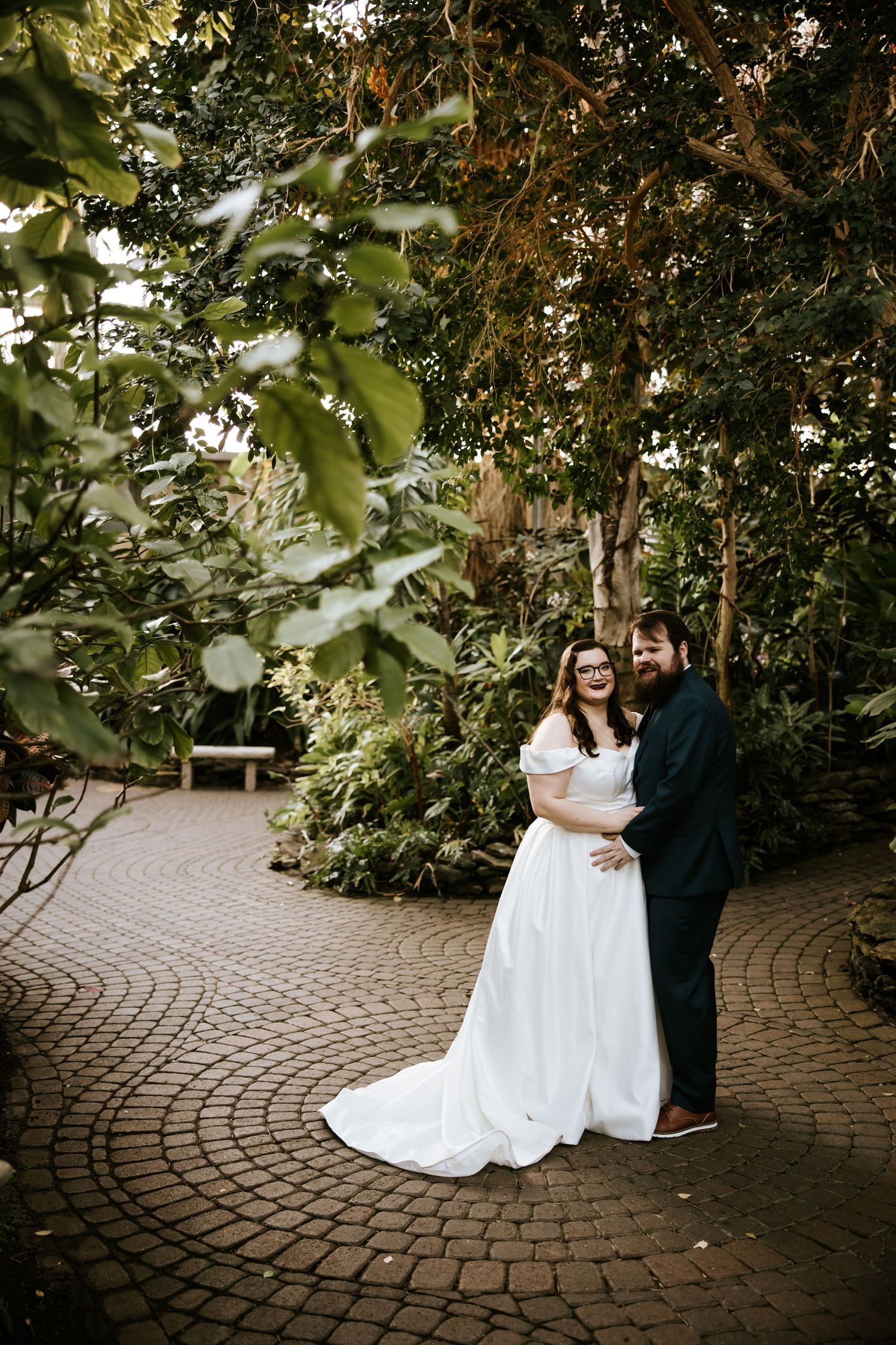 Couple shares romantic moments on brick pathway surrounded by garden foliage.