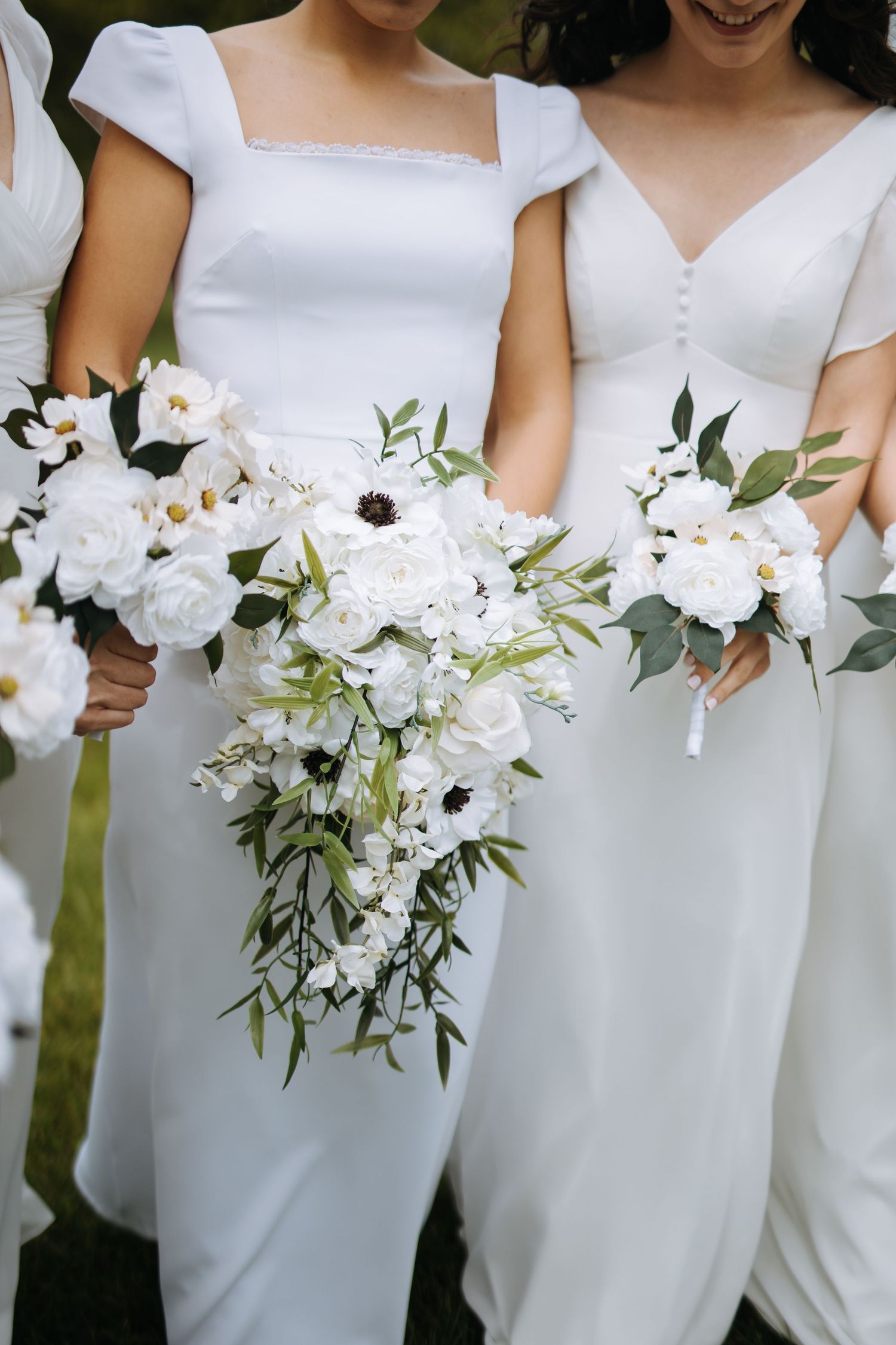 A row of white wedding bouquets held against elegant white bridesmaid dresses.