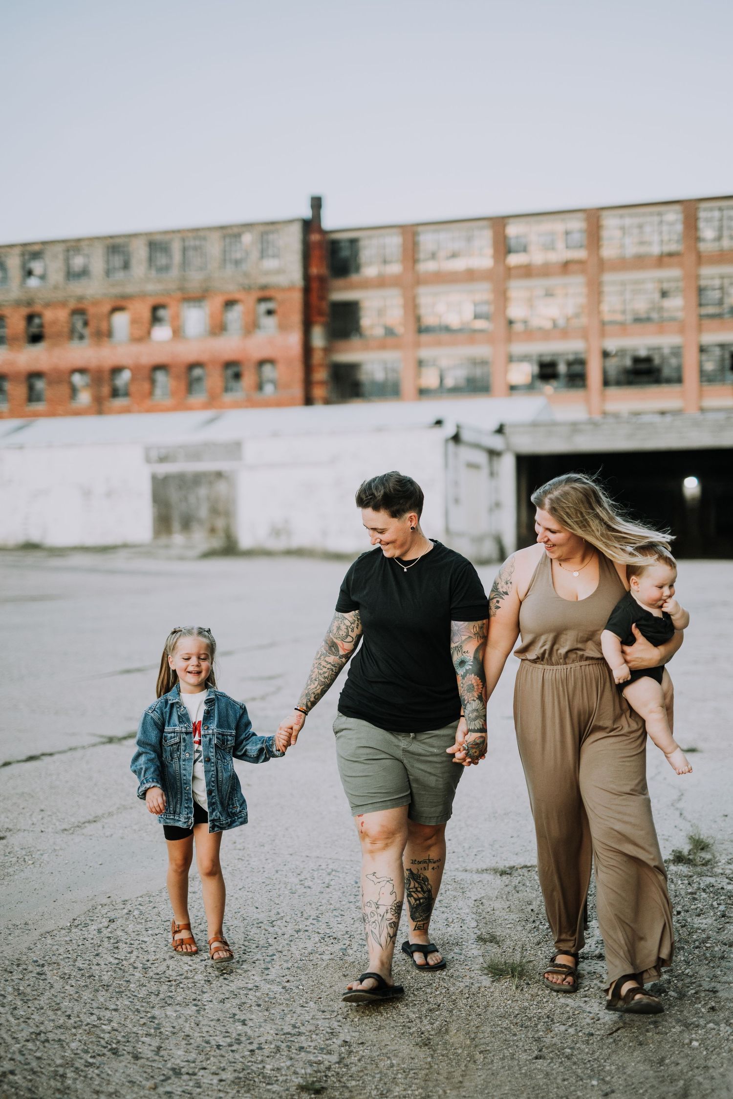 Family walking together on gravel path by industrial buildings.