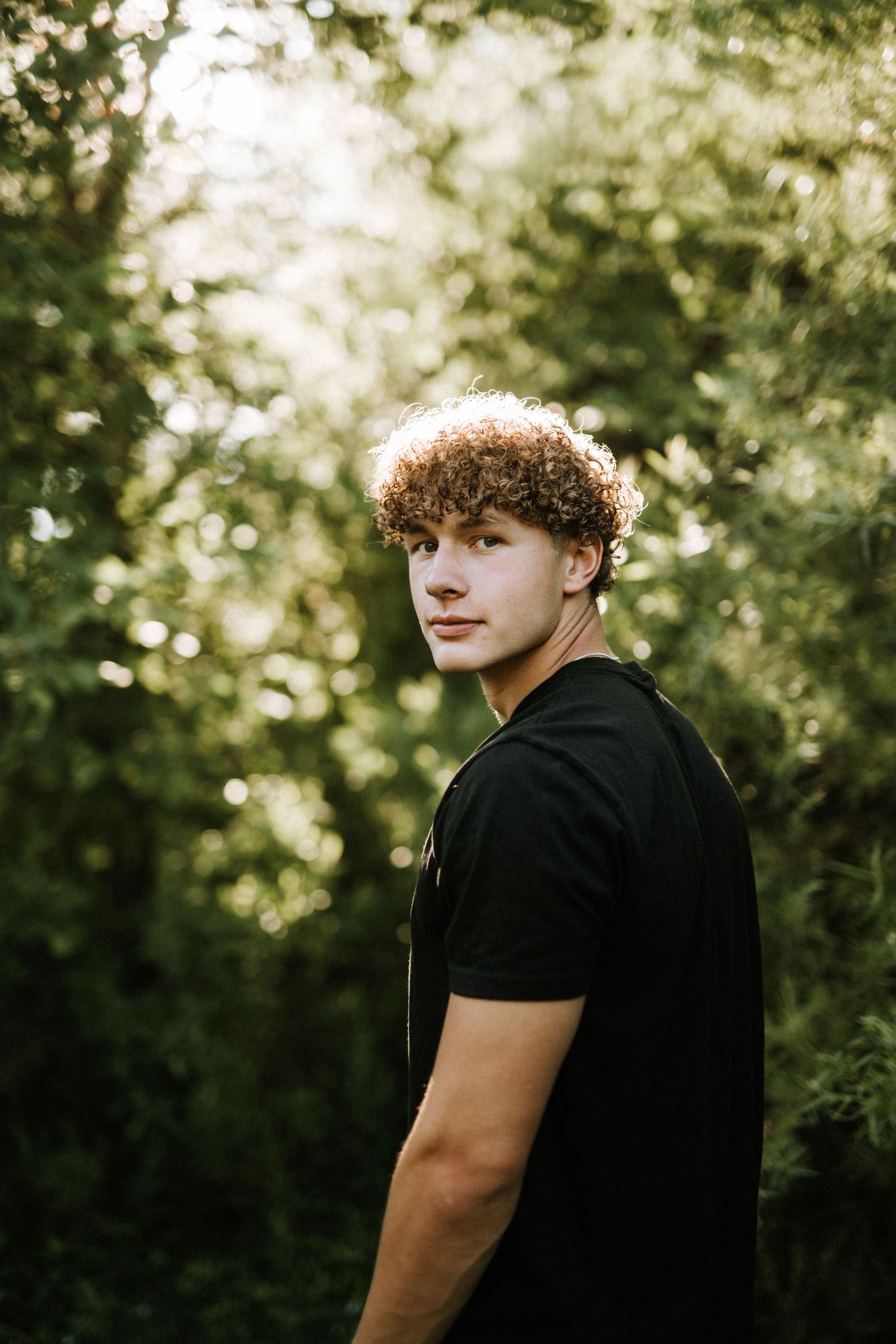 Portrait in black clothing against a backdrop of green foliage.