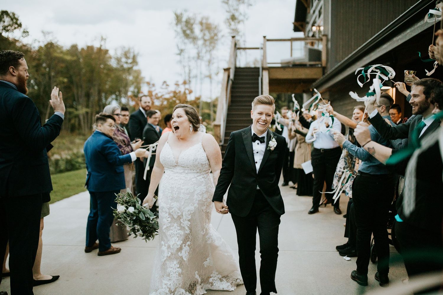 Wedding guests celebrate and cheer with bubbles as newlyweds exit their outdoor ceremony.