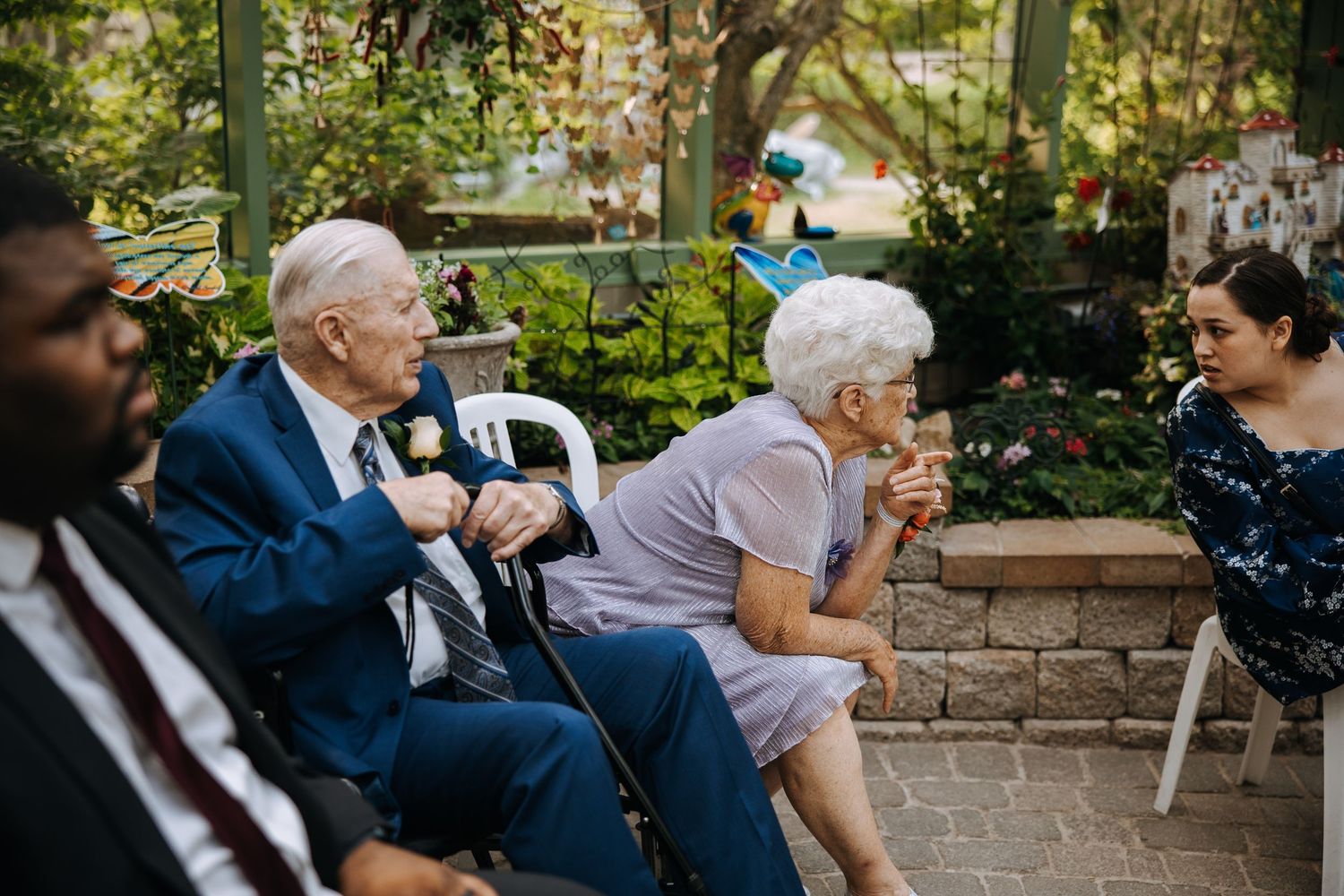 Wedding guests seated in an outdoor garden venue with stone walls.
