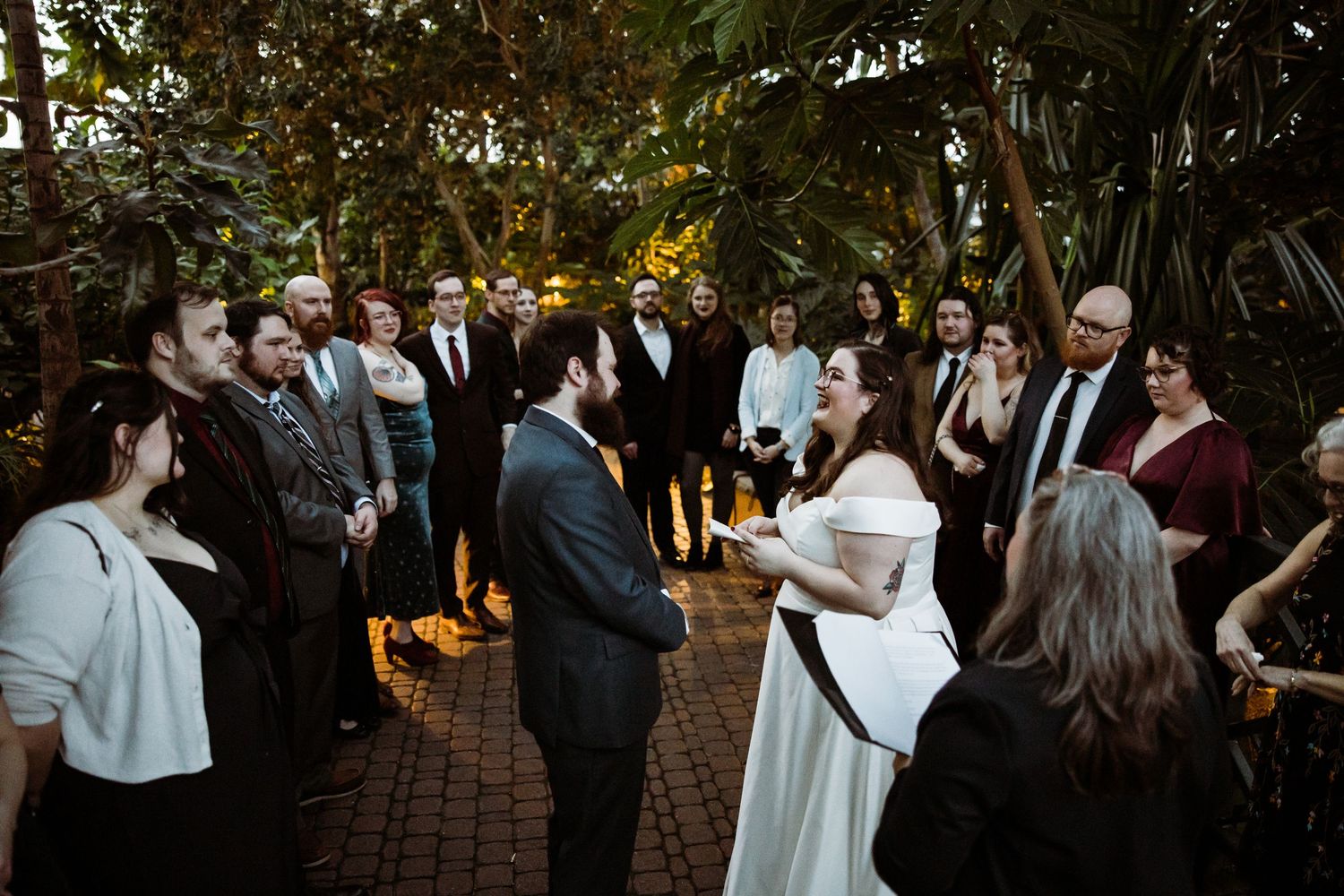 Wedding guests gathered around a couple during an outdoor garden ceremony.