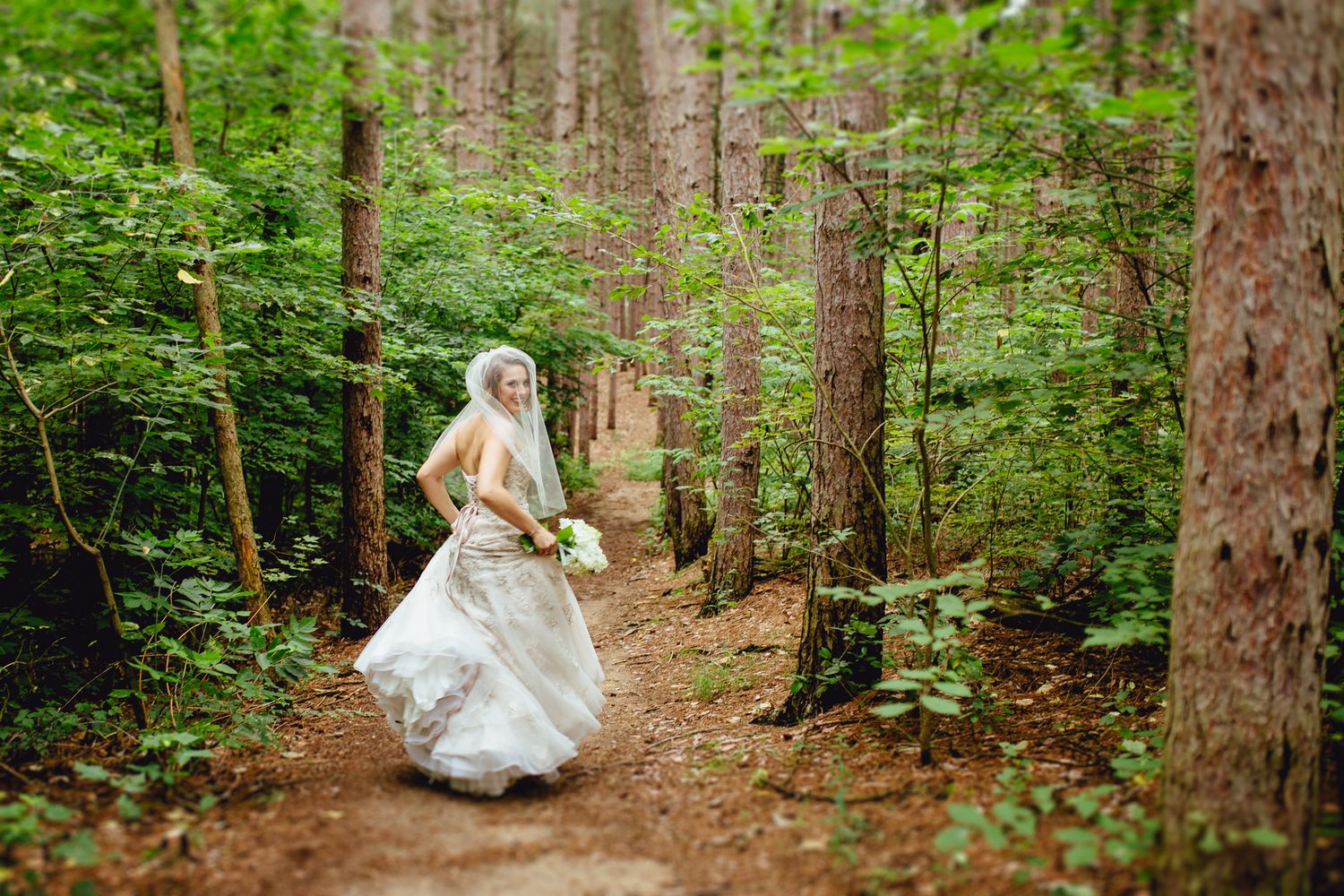 Wedding couple walking through a lush green forest path.